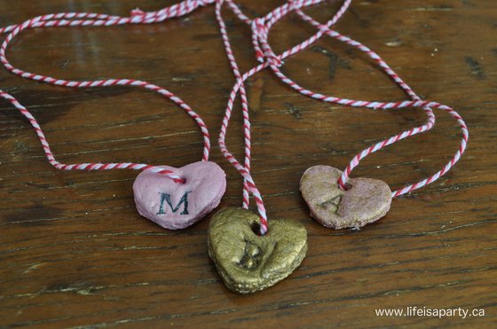 three salt dough valentine necklaces in pink and gold with a letter stamped on them