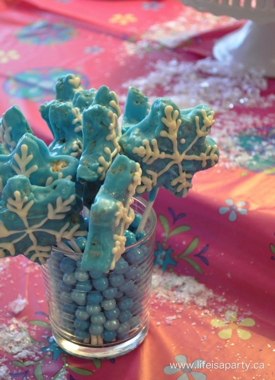 Snowflake shaped Rice Krispie treats dipped in chocolate and on a lollipop stick.