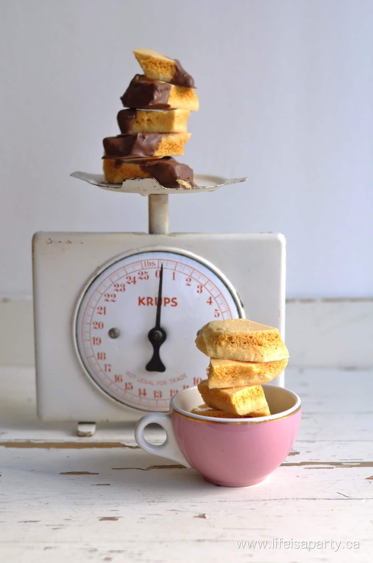 a vintage white scale with a stack of sponge candy on it, and a pink tea cup in front with more toffee in it