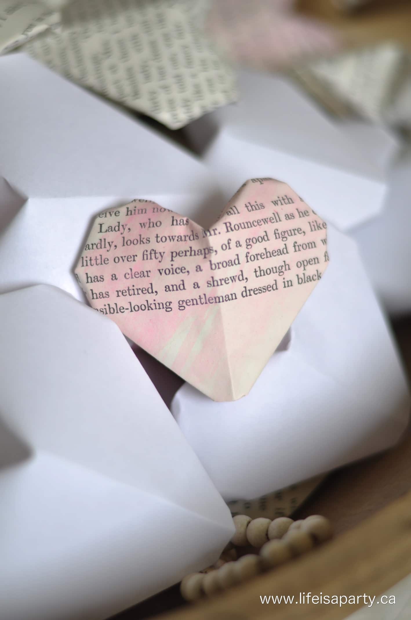 A 3d origami heart made from an old book page watercolored soft pink.