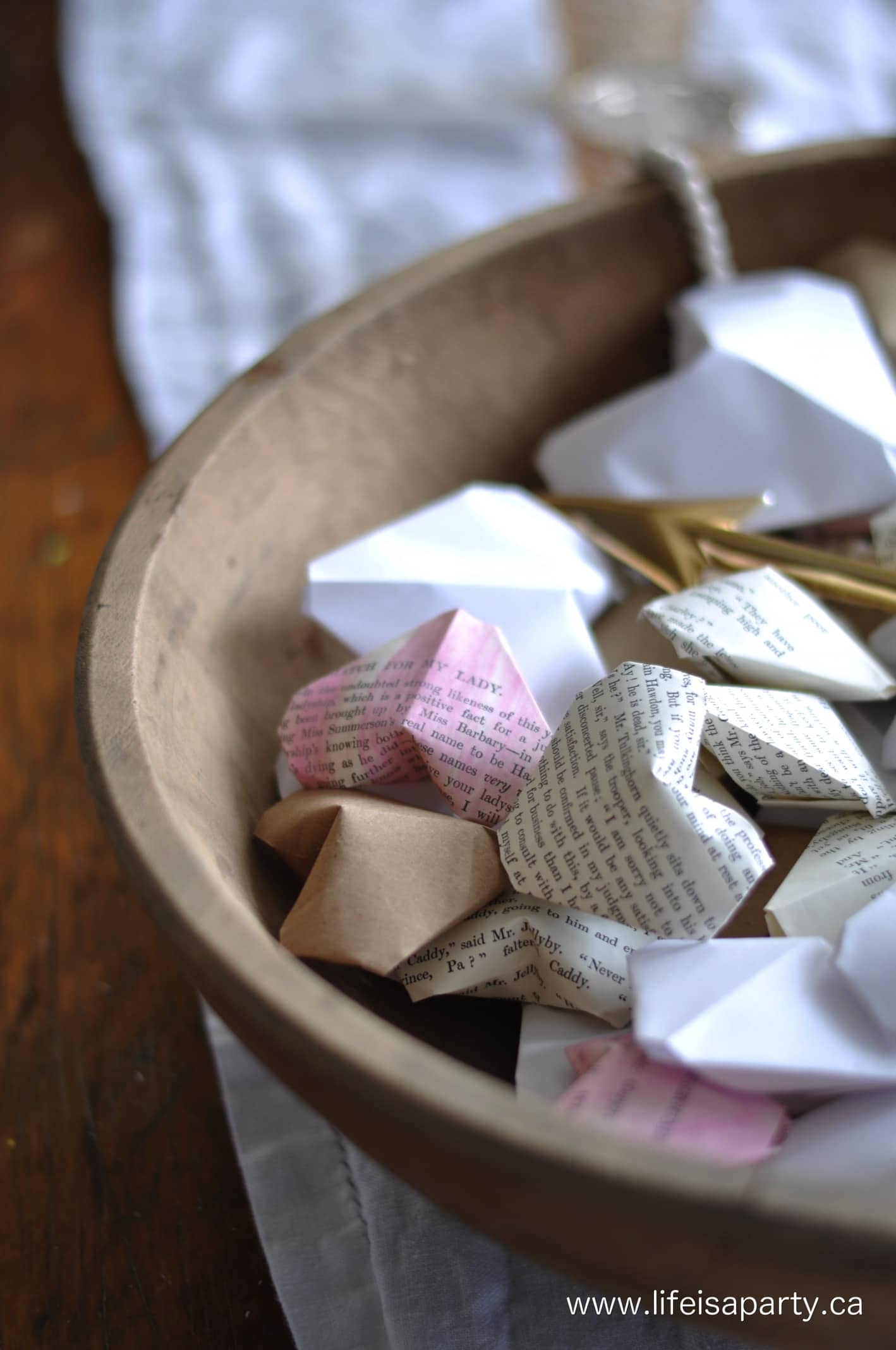 The edge of a large wooden dough bowl filled with paper hearts in white, brown and soft pink.