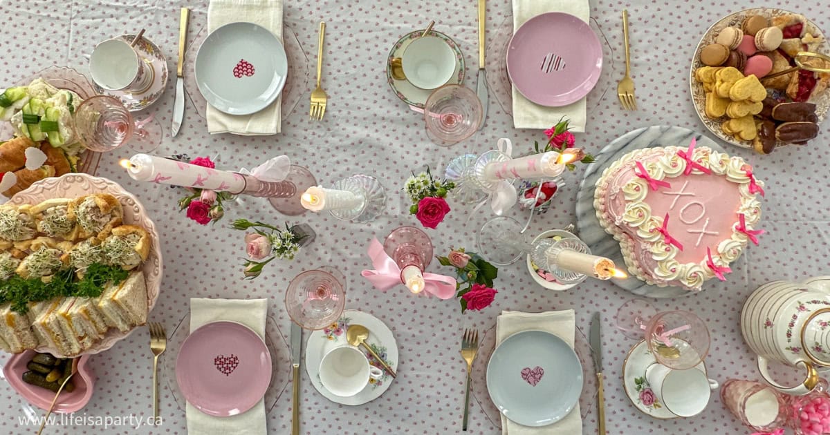 Valentine's Day tea party table with pink tablecloth, flowers, and food.