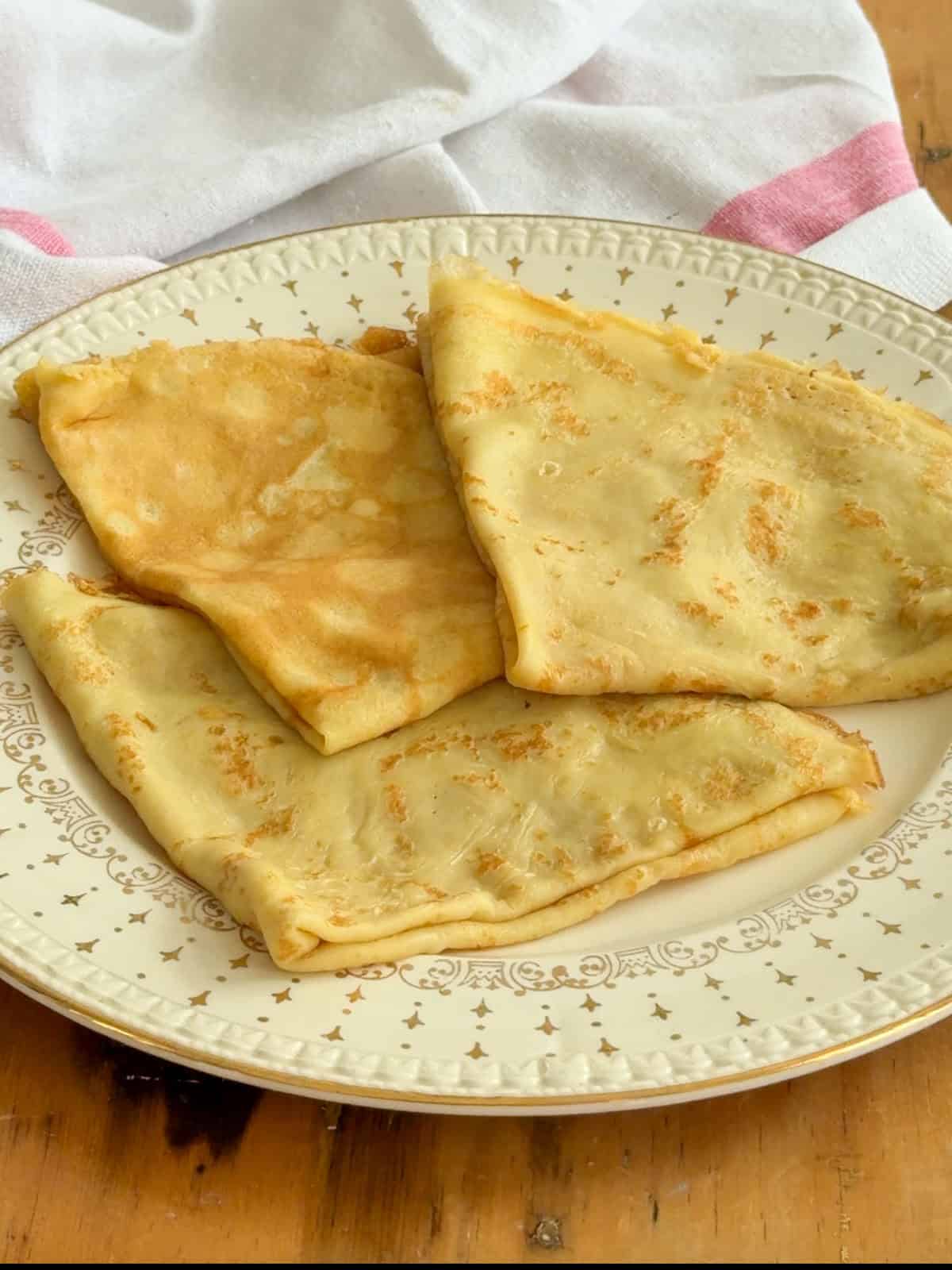 A golden sweet crepe cooked through and ready to fold, shown on a vintage star-patterned plate.