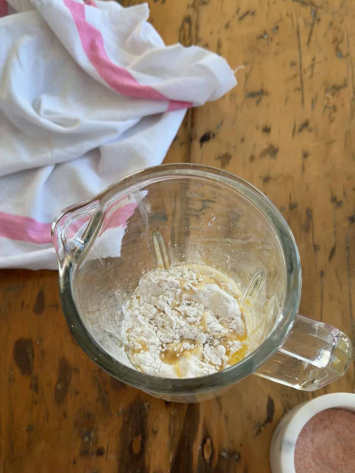 Sweet crepe ingredients including flour, eggs, and melted butter added to a glass blender jar before blending.