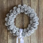 Finished DIY pinecone wreath with white spray paint and ribbon for fall or Christmas décor.