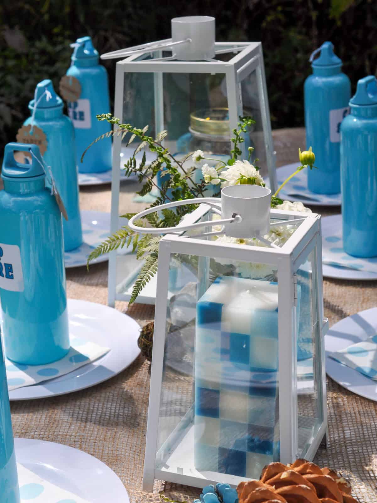 Camping birthday party table set with aqua water bottles, polka dot plates, and white lanterns.