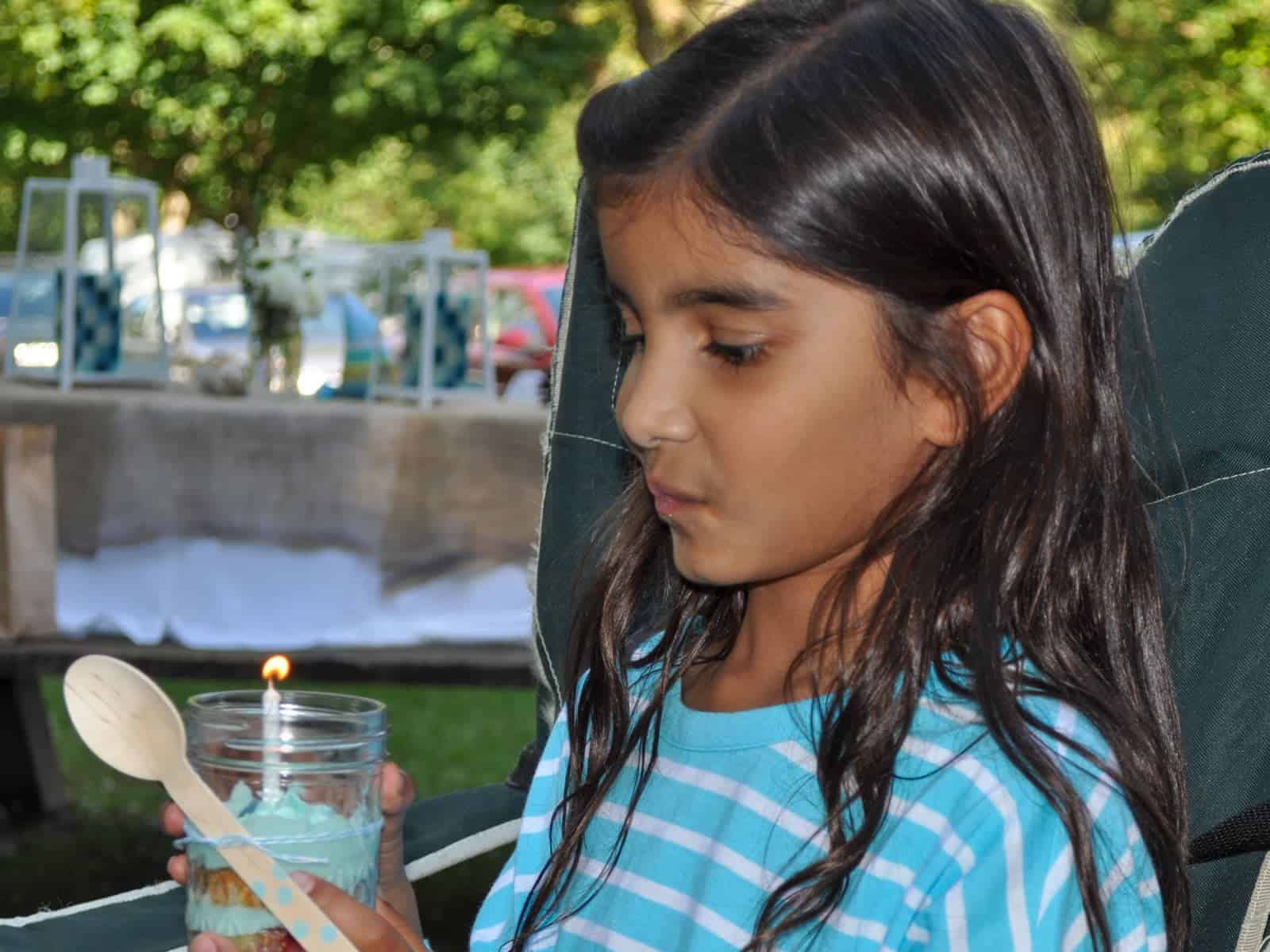 Birthday girl blowing out a candle on her cupcake in a jar at a camping party.