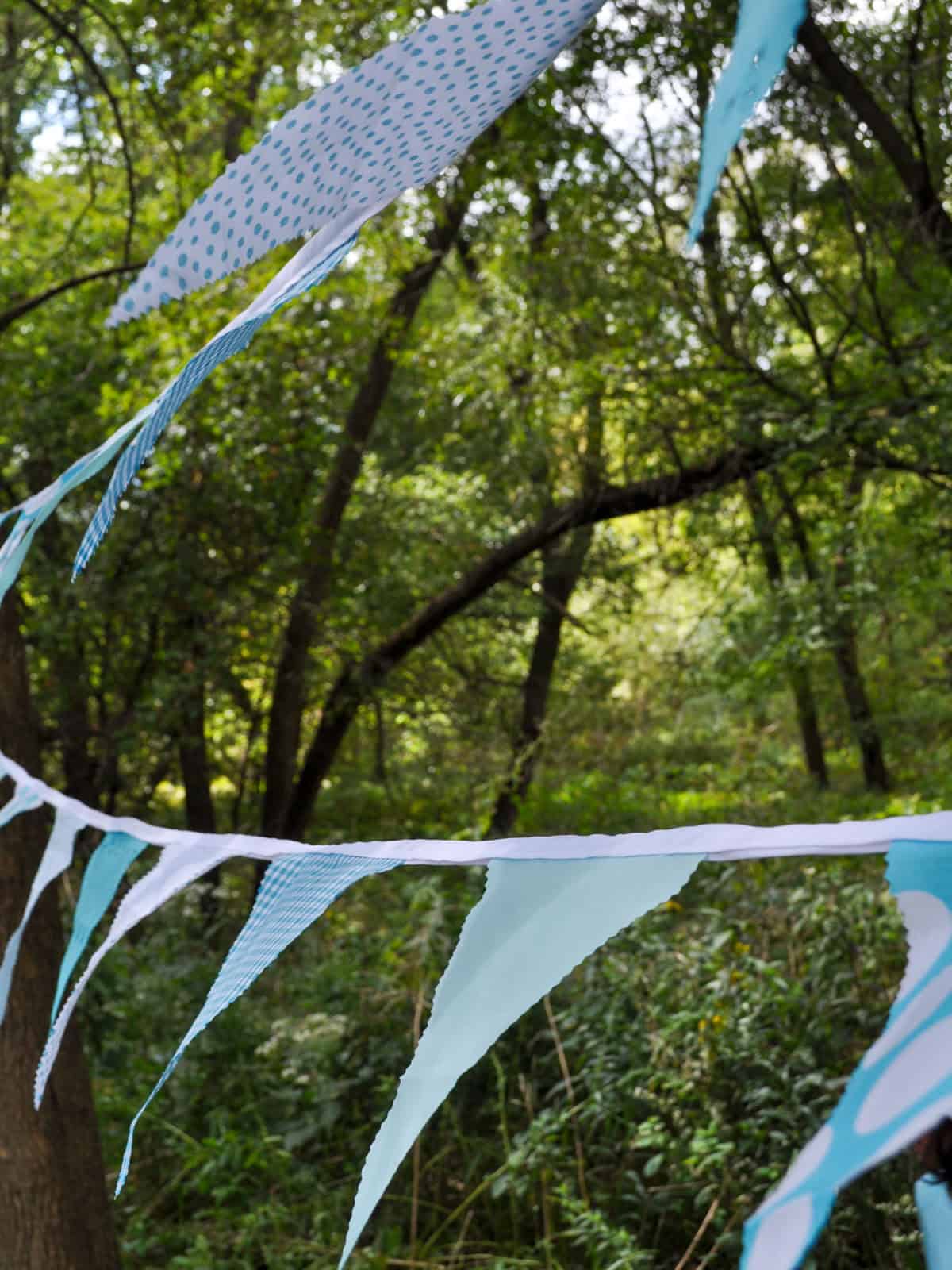 Aqua and white fabric bunting flags strung between trees at a camping birthday party.