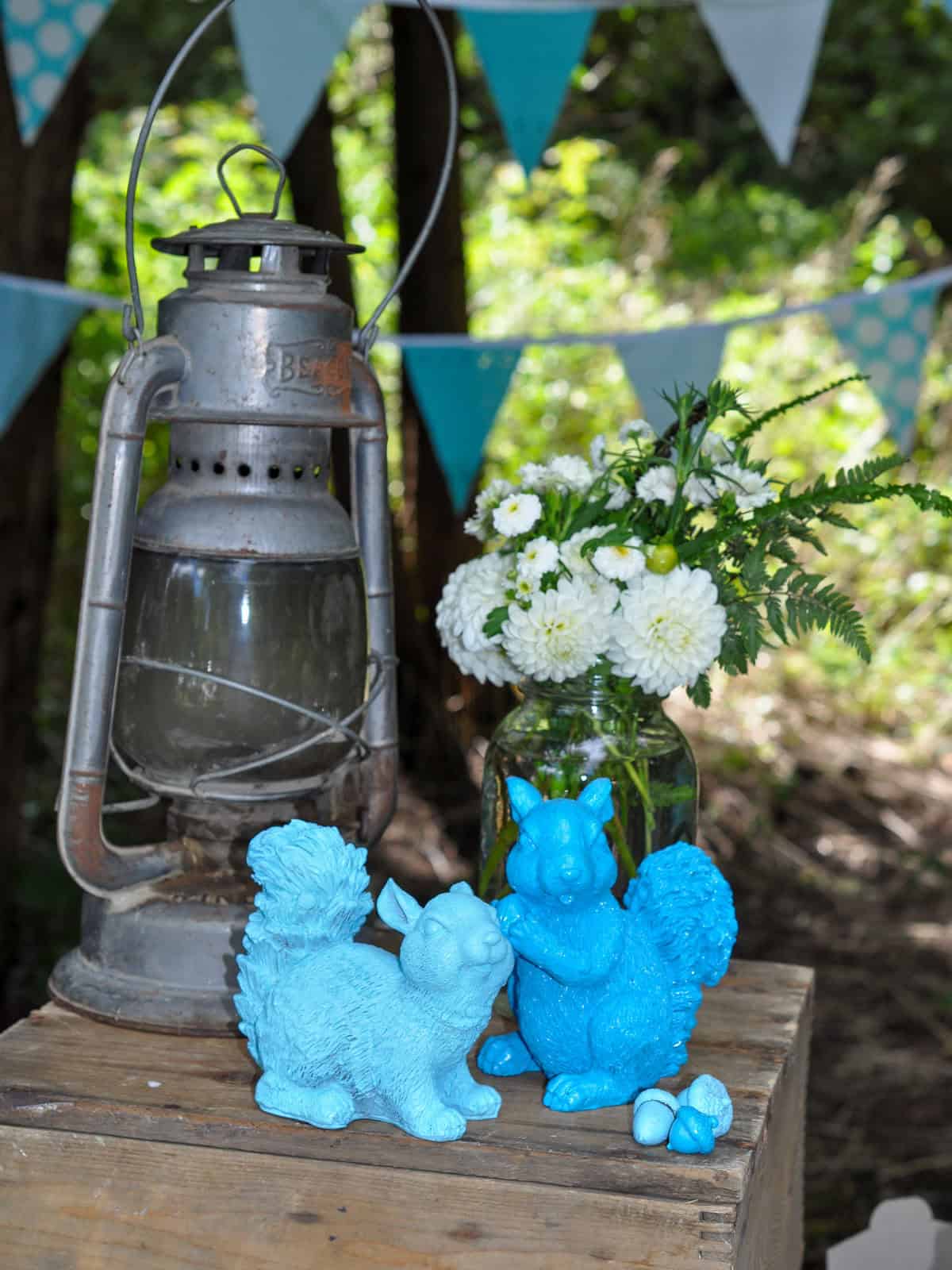 Vintage lantern displayed with aqua spray painted squirrel figurines on a wood crate.