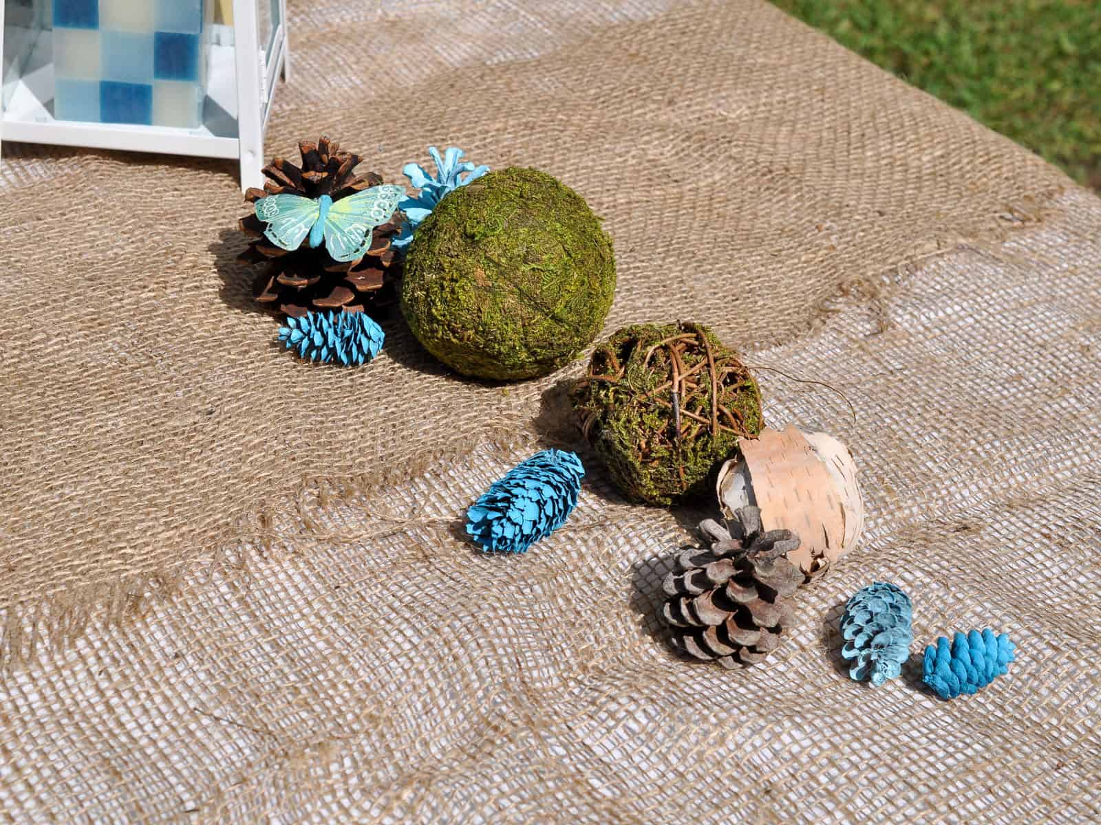 Natural table runner made of moss balls, pinecones, and birch bark for a camping party centerpiece.