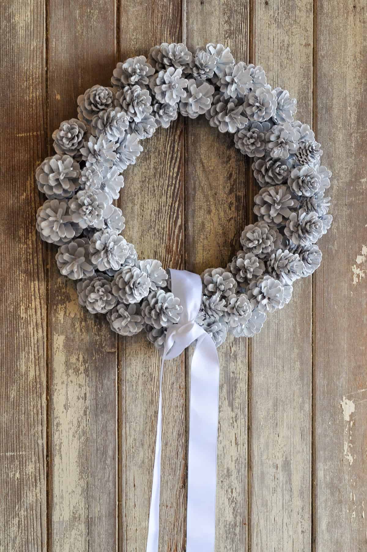 White DIY pinecone wreath with long white ribbon.