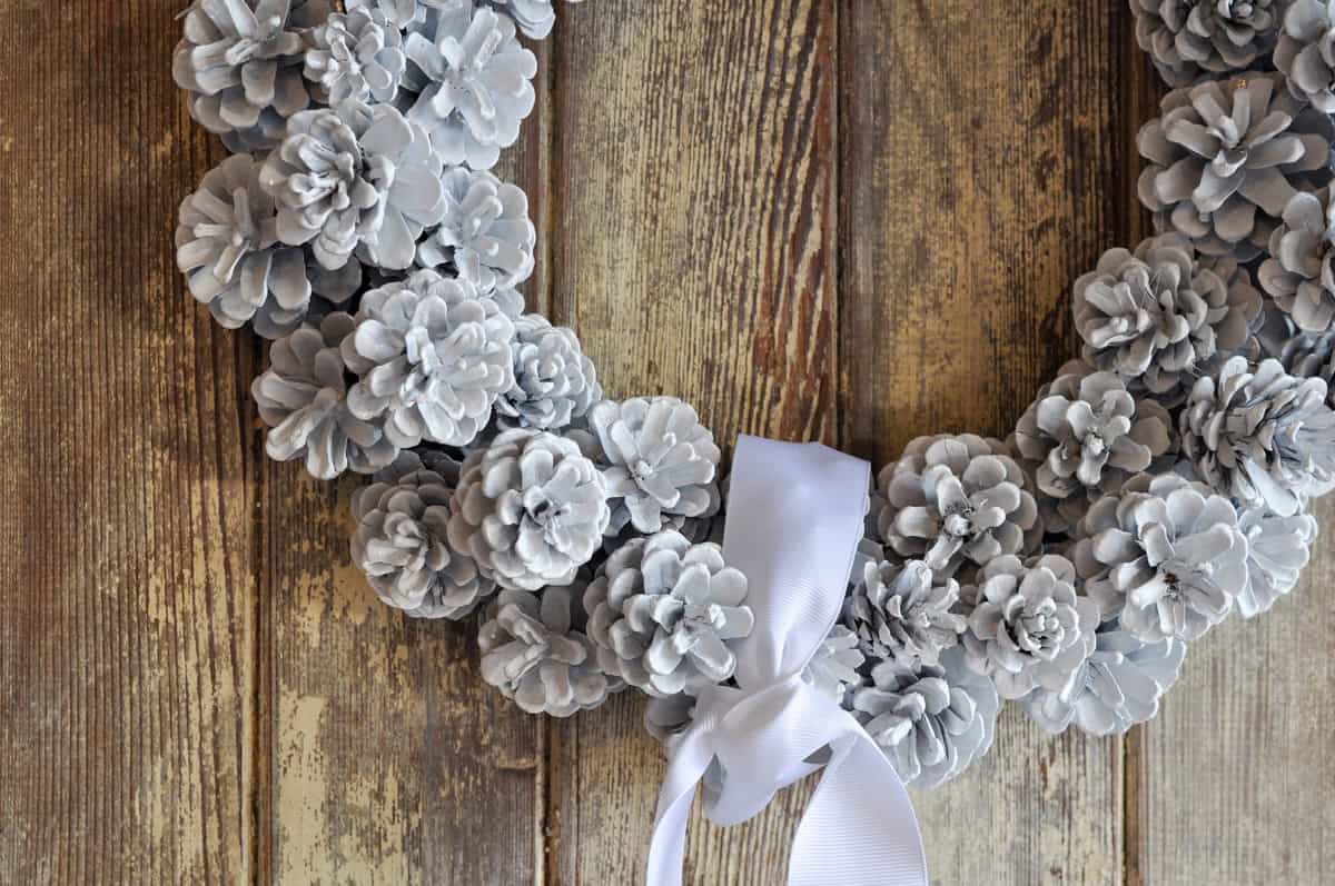 DIY pinecone wreath spray painted white, with a white ribbon.