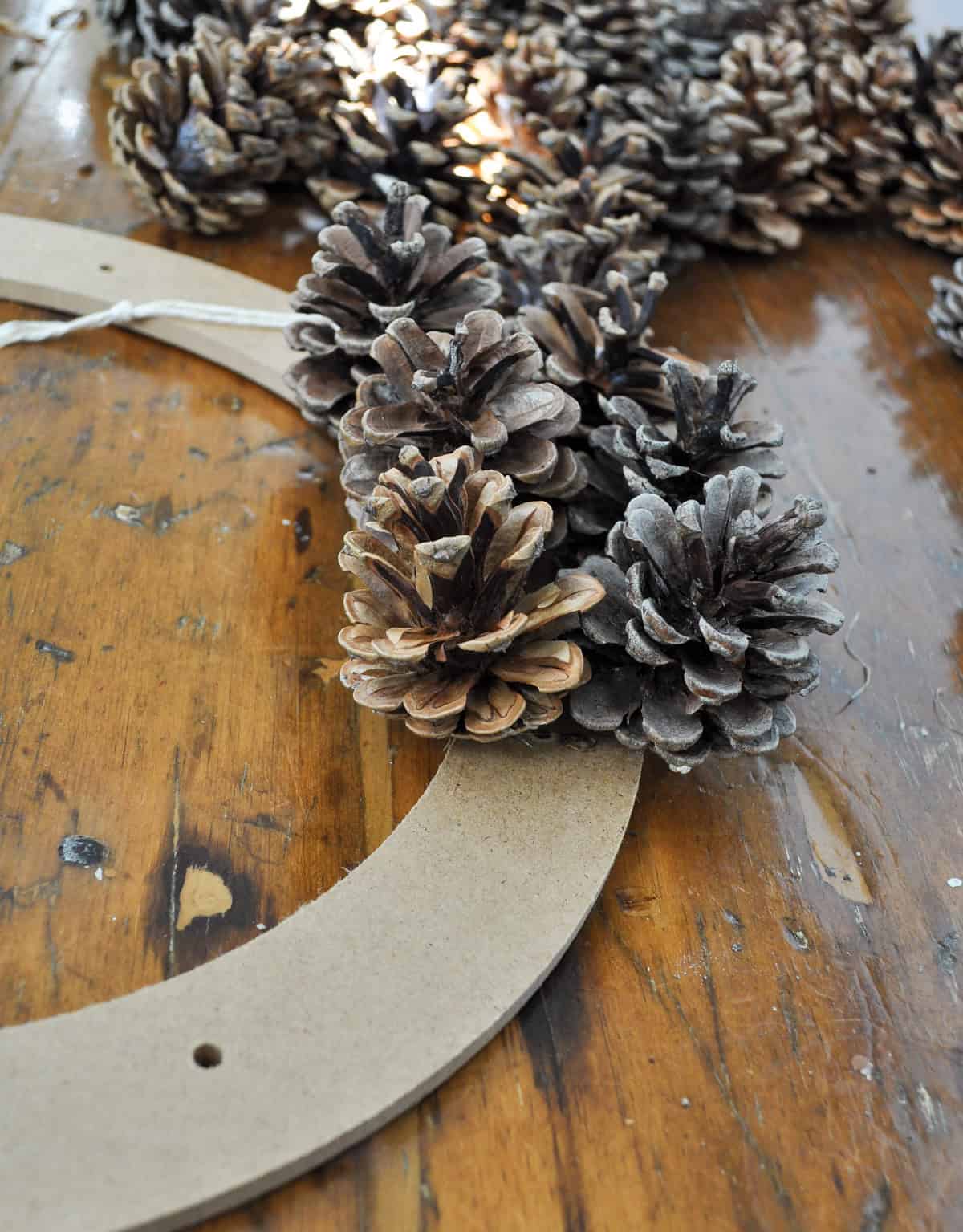 DIY tutorial showing how to make a pinecone wreath by hot gluing pinecones to a wooden base.
