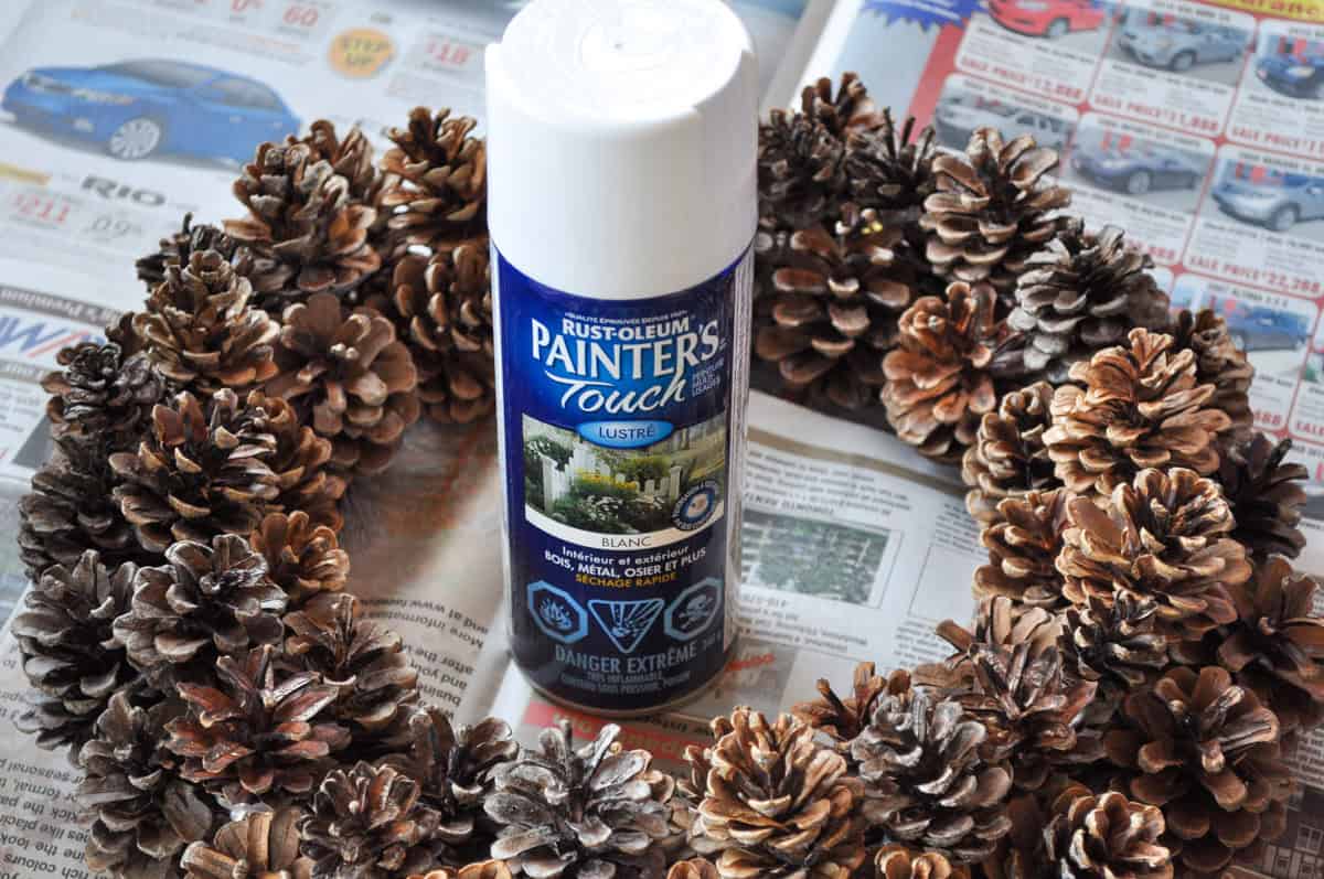 Can of white spray paint in a round DIY pinecone wreath.