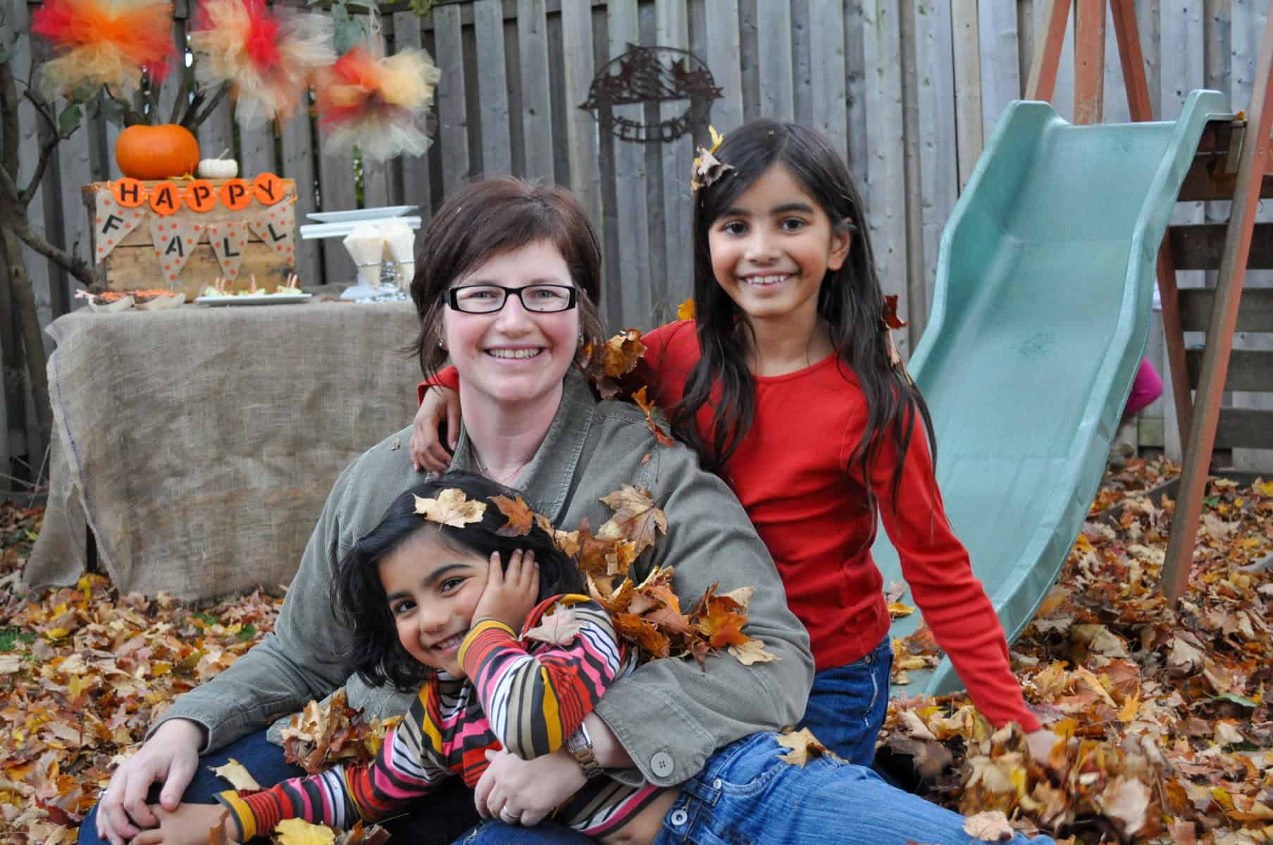 People at a fall party raking and playing in the leaves.