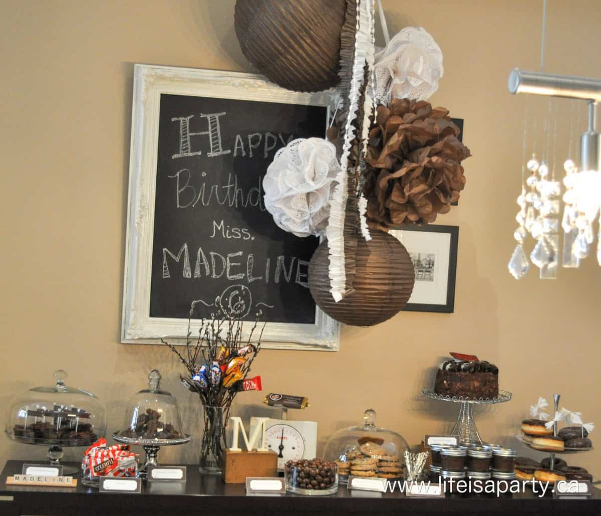 Chocolate dessert table with paper lanterns and tissue paper balls hanging over it.