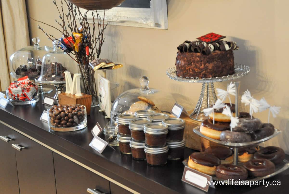 Chocolate themed dessert table with pudding, cake, donuts, cookies and more.