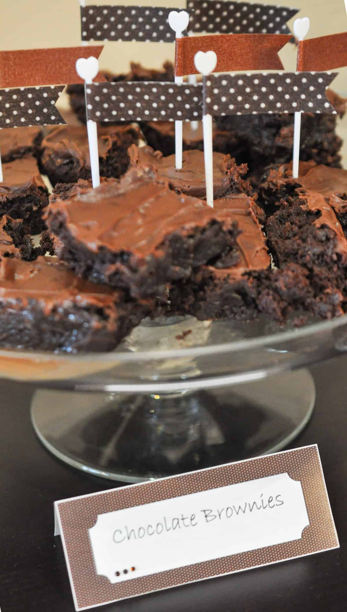 Chocolate brownies on a cake plate with brown washi tape flags in them.