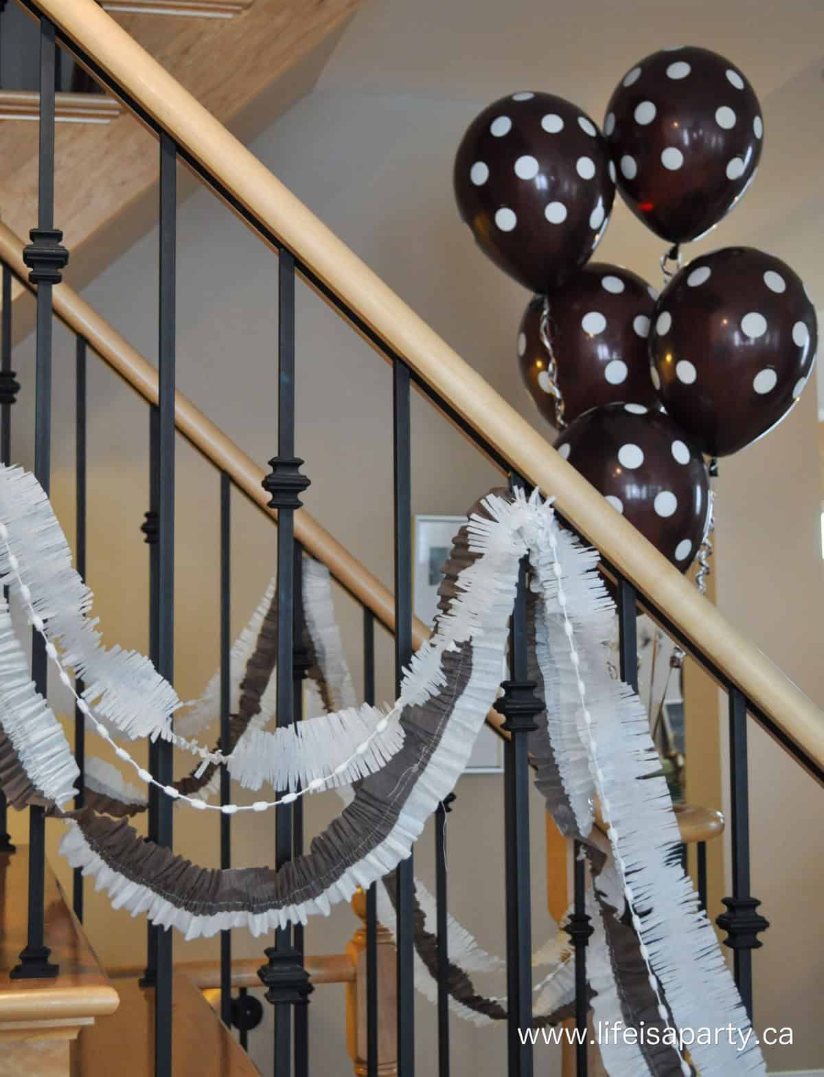 Chocolate themed party decorations of brown and white streamers and polka dot balloons on stairway.