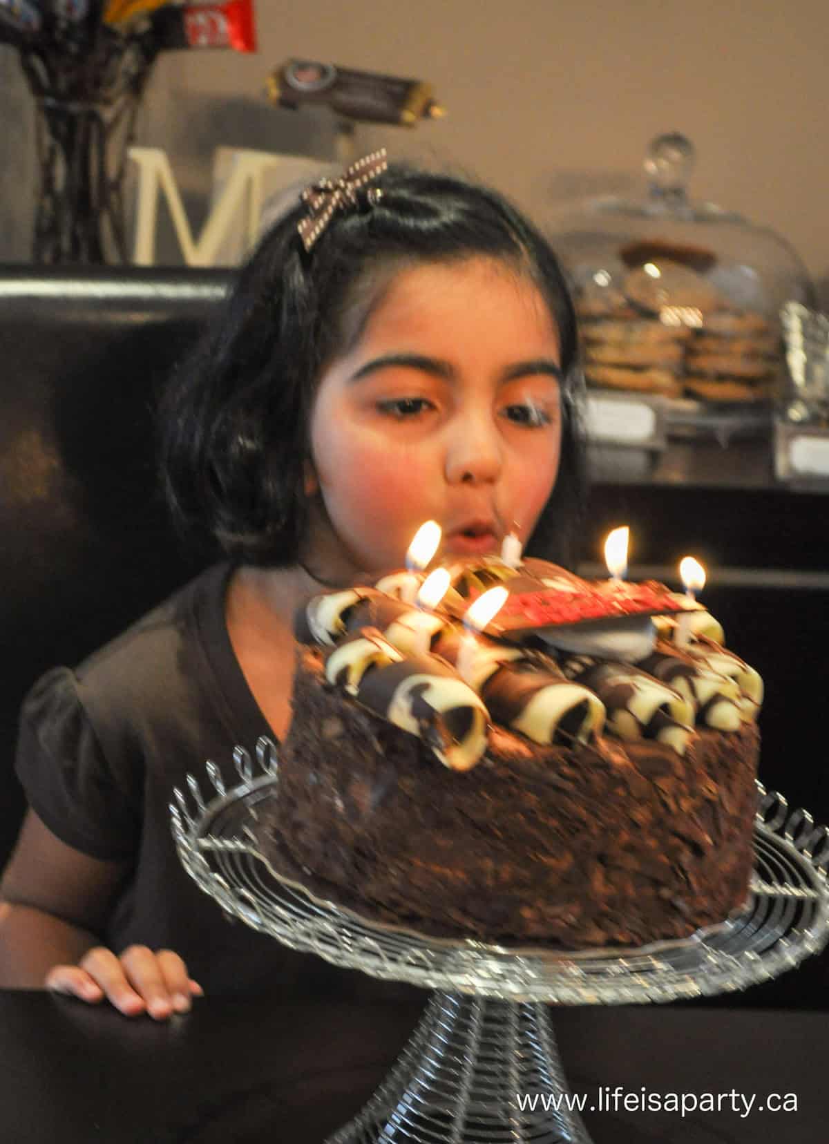 Child blowing out candles on a chocolate birthday cake.