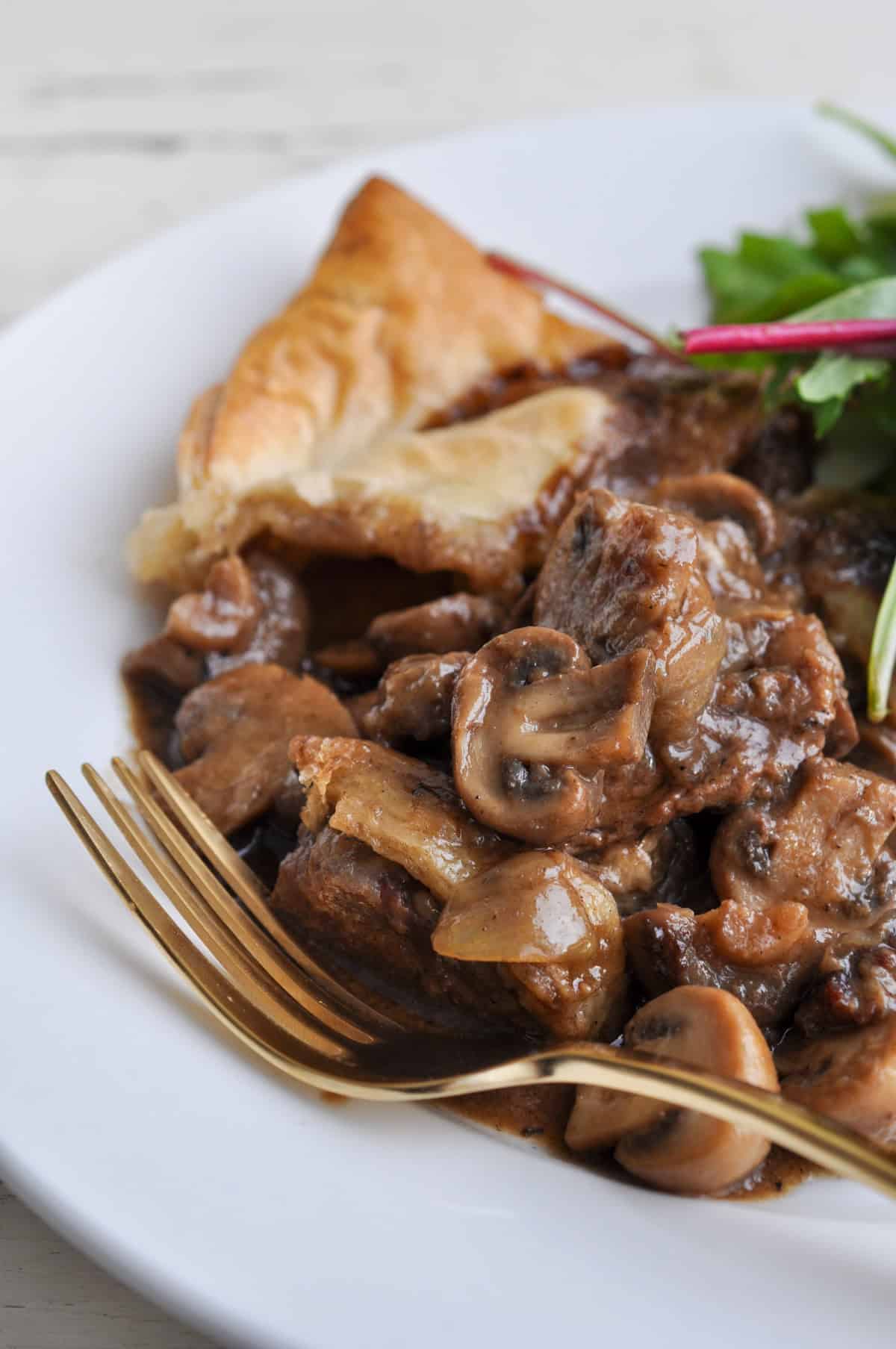 Plated steak Guinness and mushroom pie with golden brown puff pastry revealing hearty beef and mushroom filling in rich gravy.