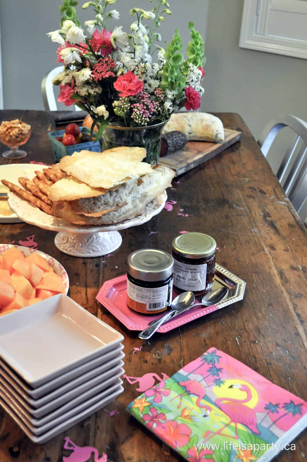 Cheese, cracker, and charcuterie appetizers for a flamingo themed party on a wood table with flowers and napkins.