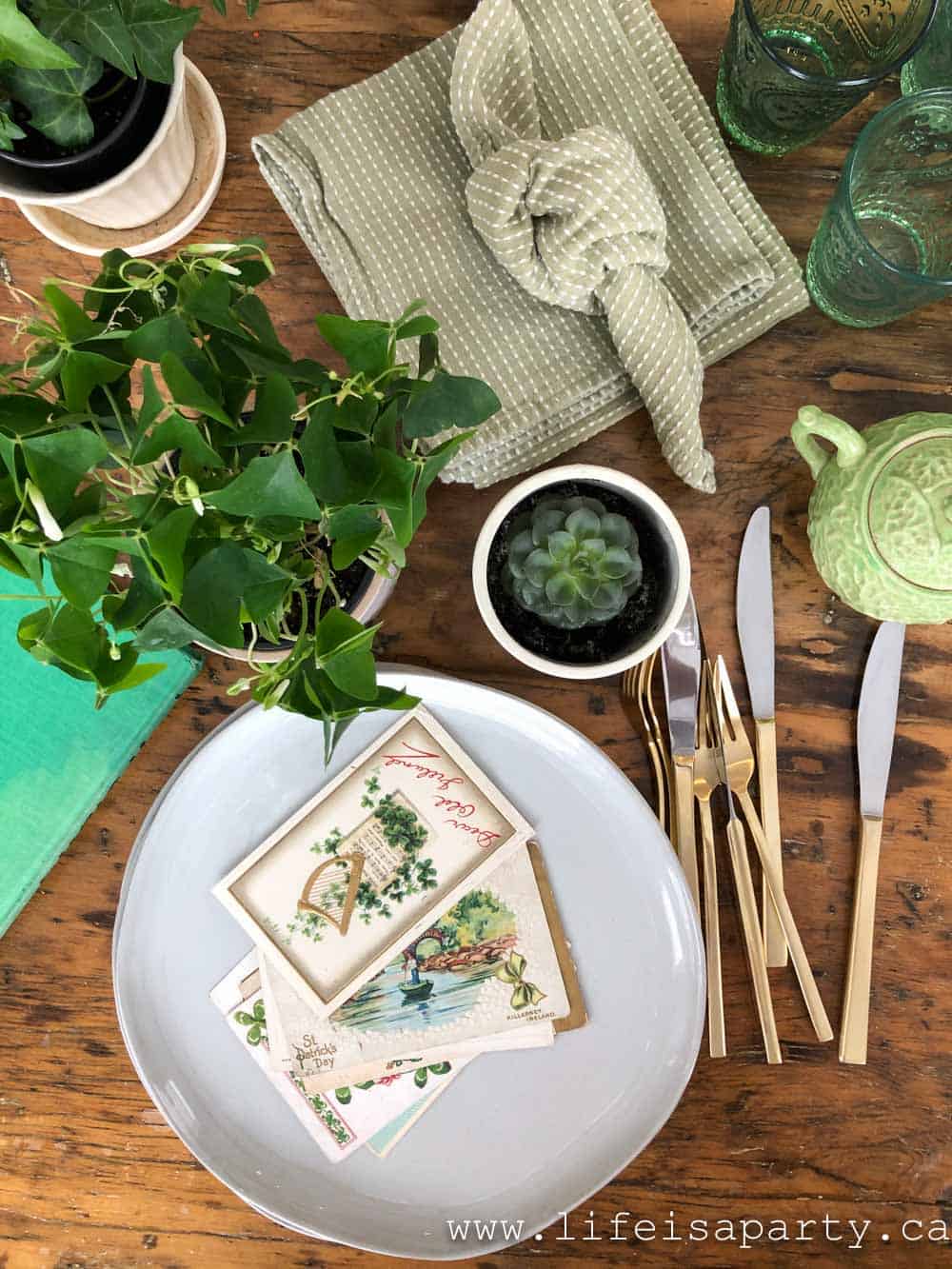 St. Patrick's Day tablescape with vintage Irish figurines, shamrock plants, green glassware, and rustic linen runner.