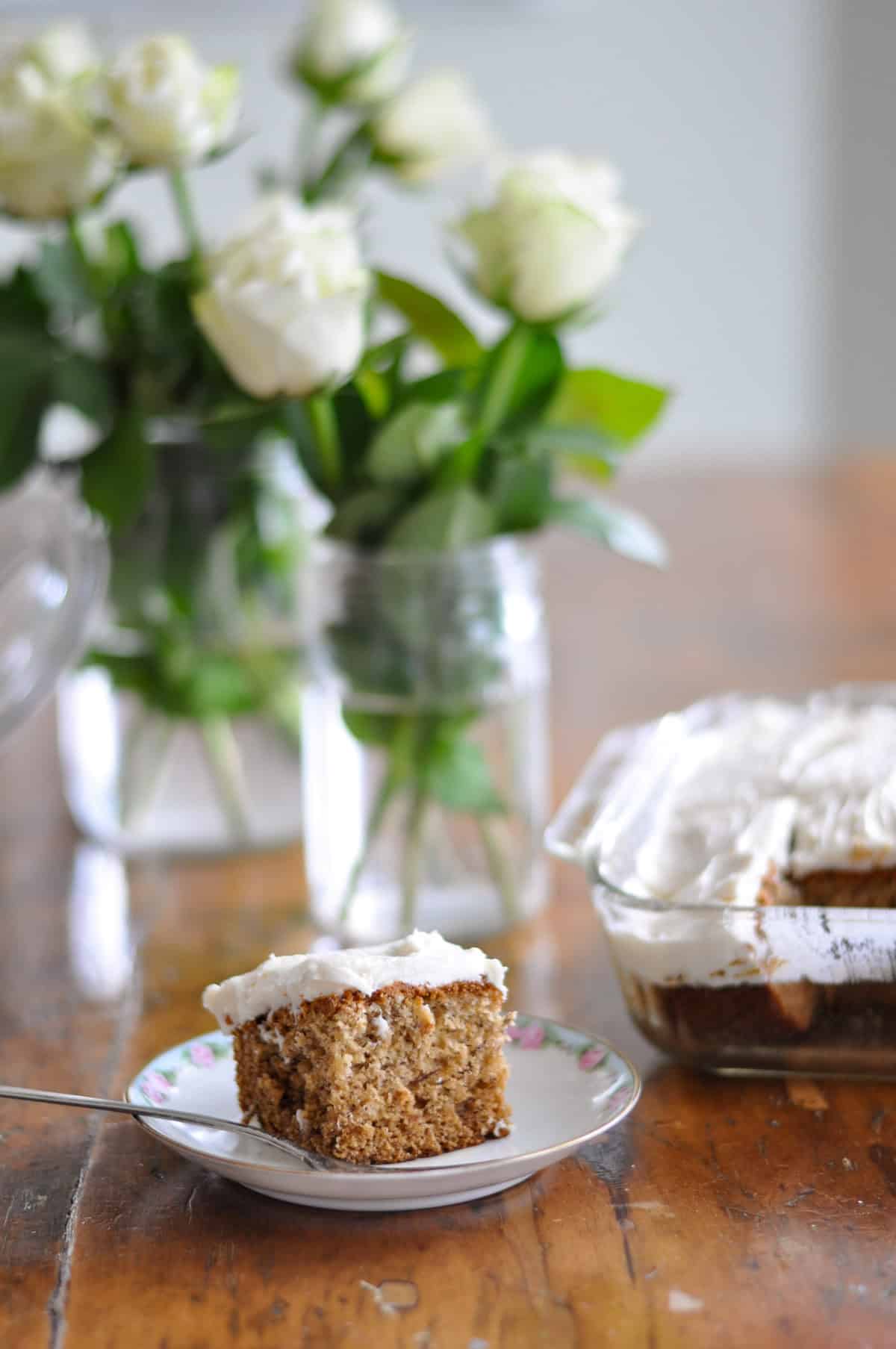bananna cake 1.jpg Easy bananana snack cake with vanilla frosting on a plate in front of some flowers in a vase.