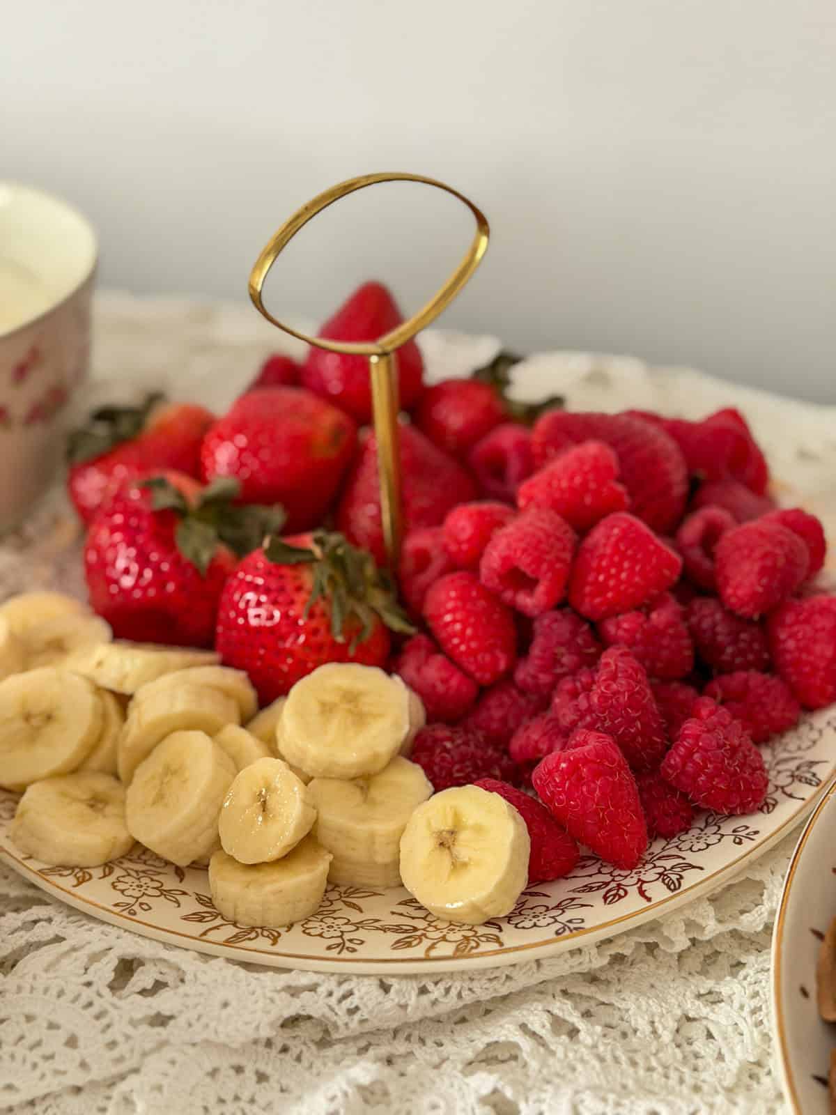 Fresh strawberries, raspberries, and sliced banana arranged on a gold-trimmed vintage china plate.