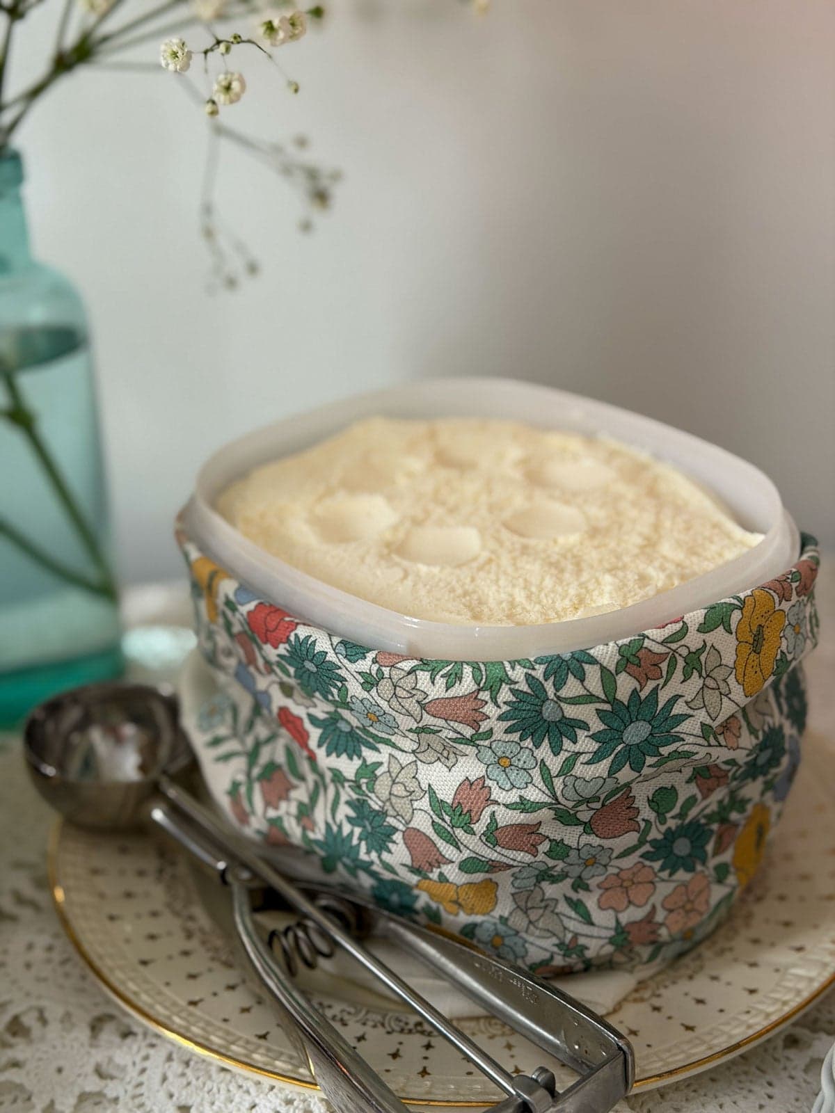 Vanilla ice cream in a Liberty floral print bowl with an ice cream scoop alongside and baby's breath flowers in the background.