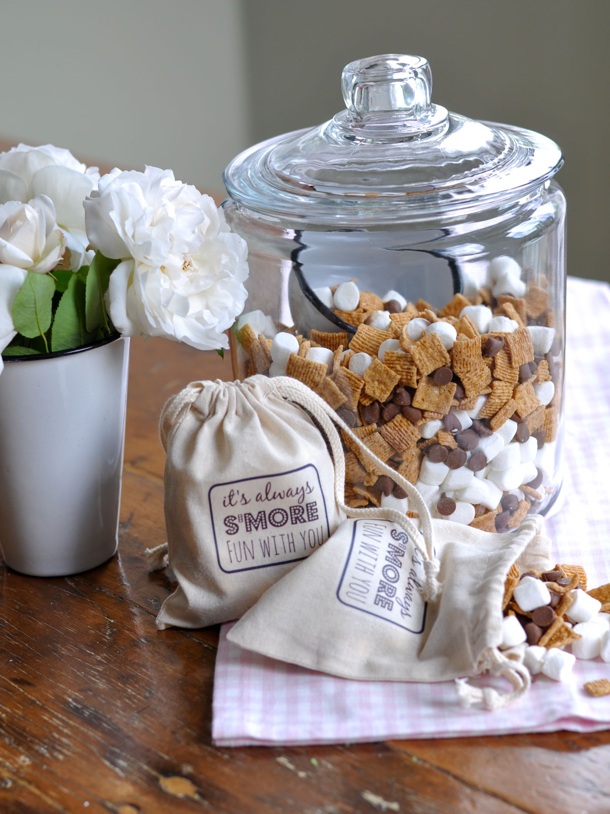 S'mores trail mix in a glass jar with two labeled canvas gift bags nearby.