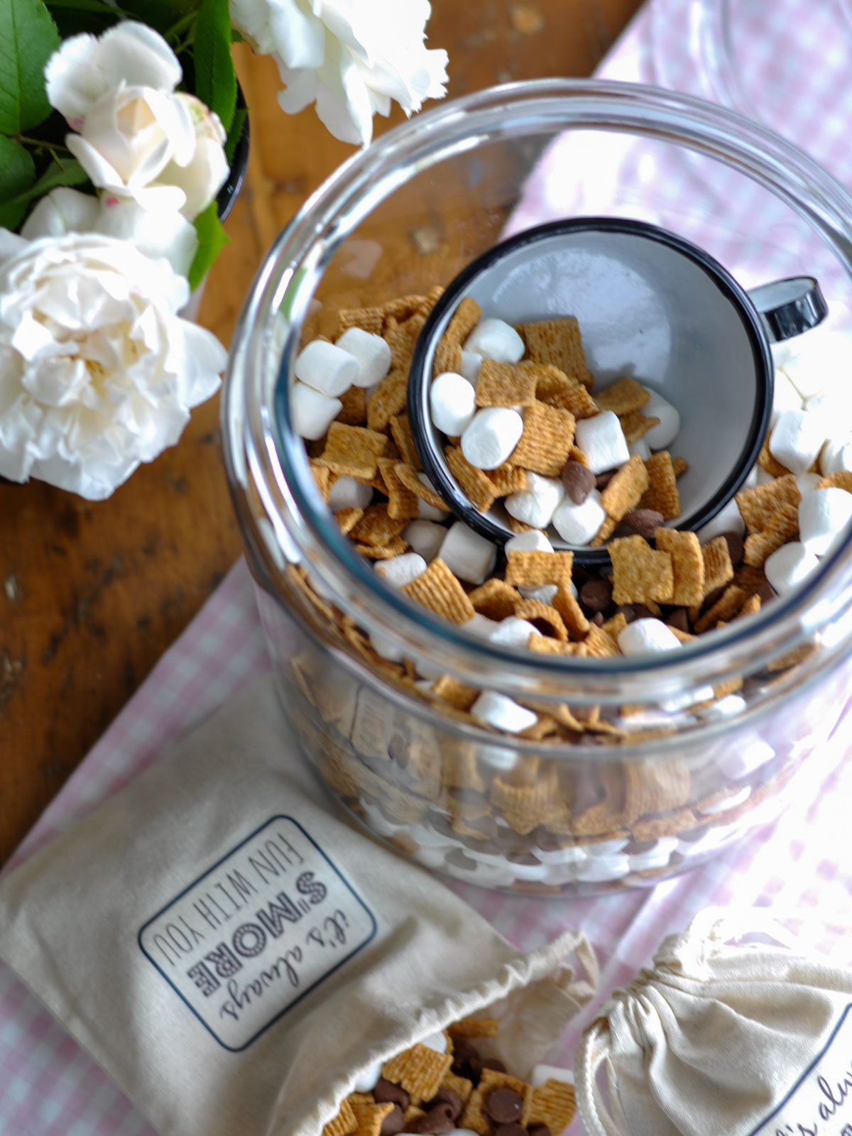 Overhead view of s'mores trail mix in a glass jar with a mug scooping out a serving.