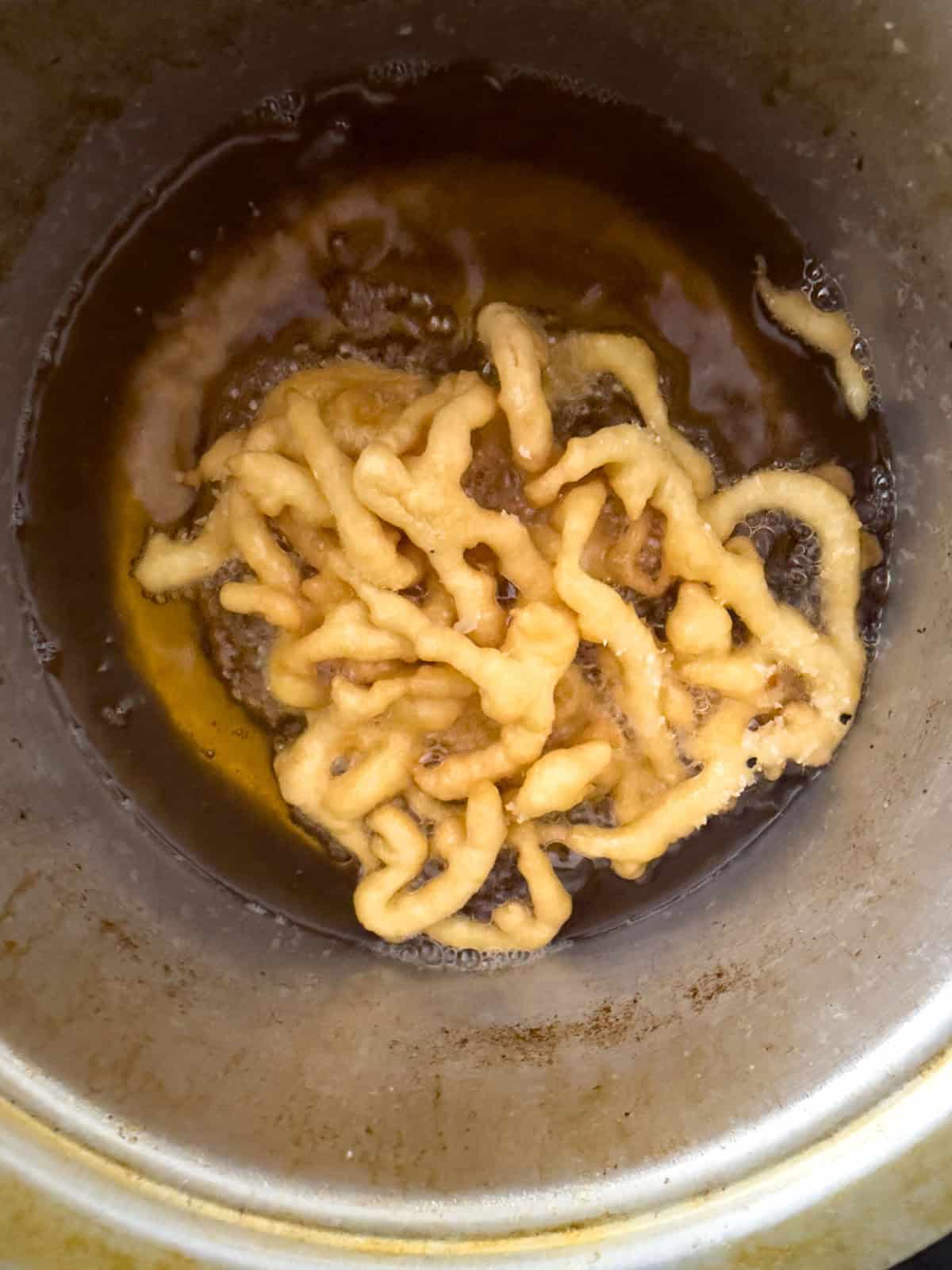 Fair funnel cake frying to golden brown in hot oil in a deep fryer.