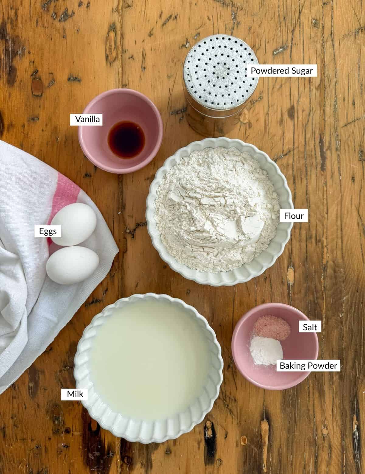 Fair funnel cake ingredients including flour, eggs, milk, vanilla, and baking powder on a kitchen table.