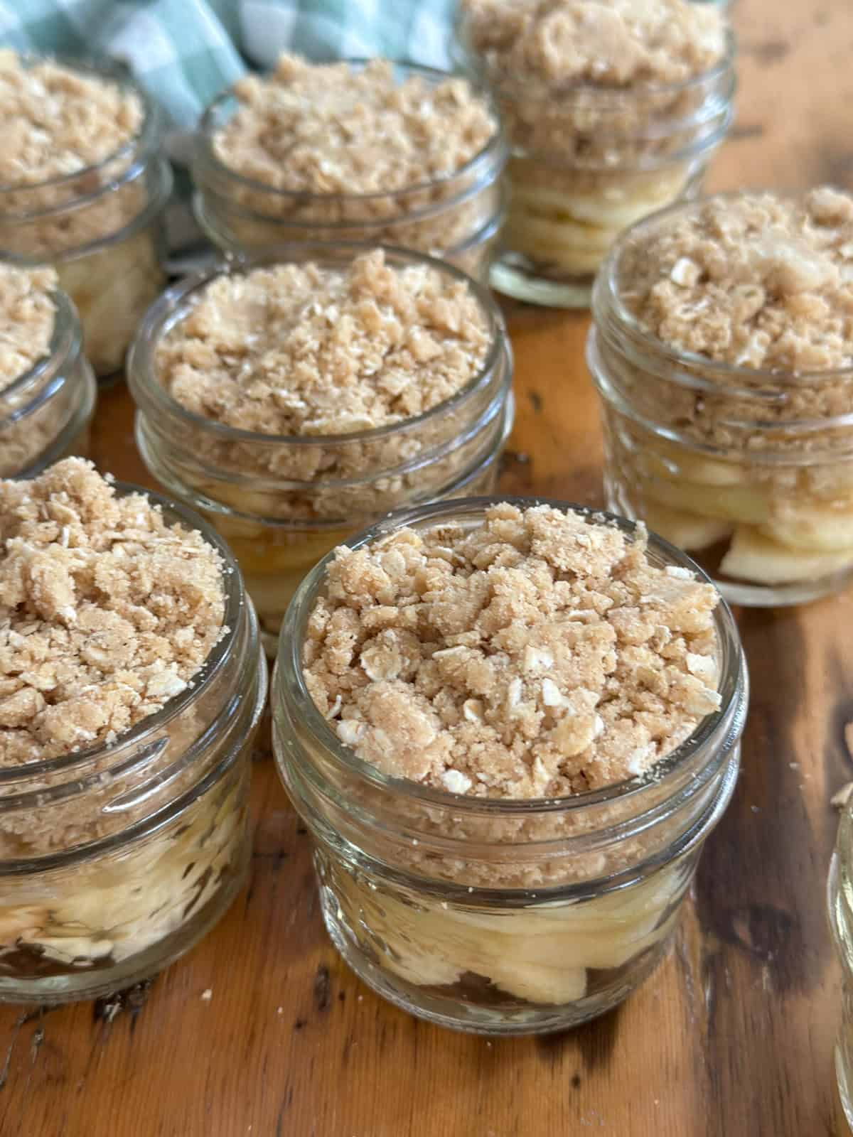 Mini apple crisps made in a mason jar with apple slices covered in crisp topping before baking.