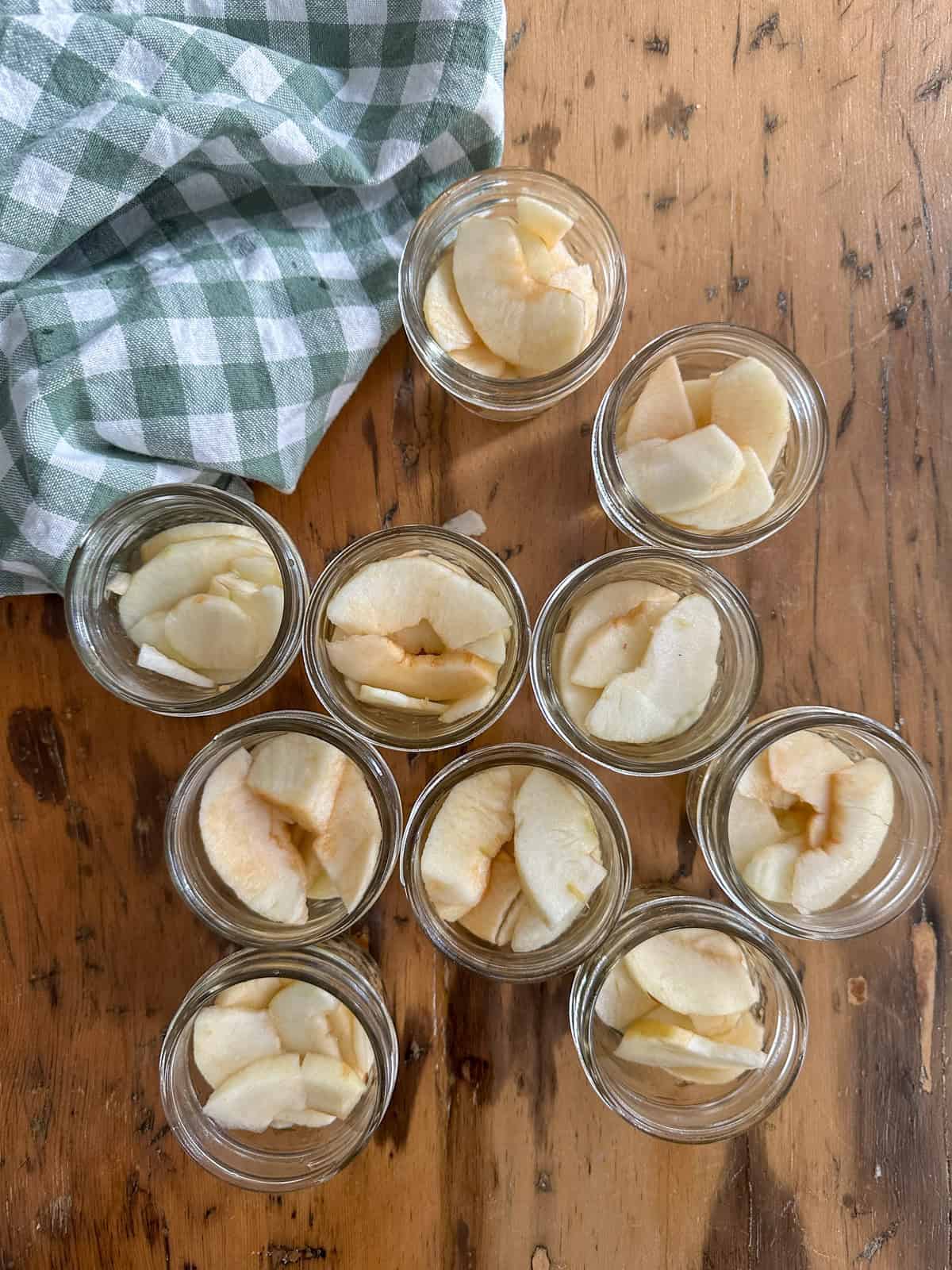 Sliced apples divided into  mini mason jars to make individual apple crisps.