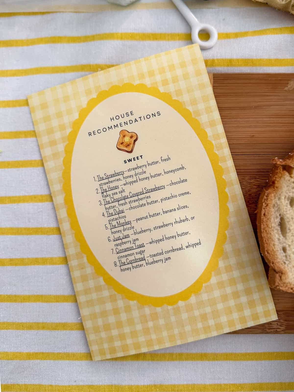 House Recommendations sweet side menu card with yellow gingham border listing eight toast combinations including The Strawberry, The Honey, The Chocolate Covered Strawberry, The Dubai, The Monkey, Just Jam, Cinnamon Toast, and The Cornbread.