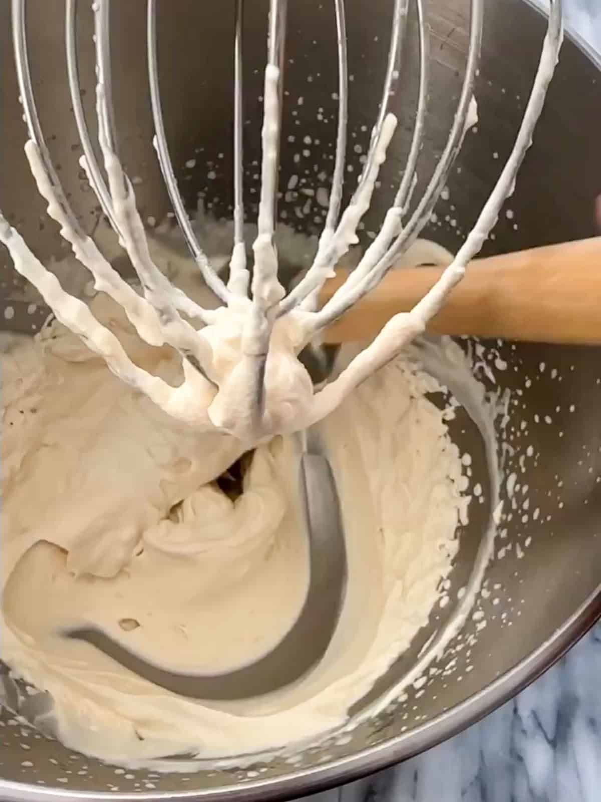 Whipped cream beaten to firm stiff peaks on a stand mixer whisk attachment for black forest trifle.