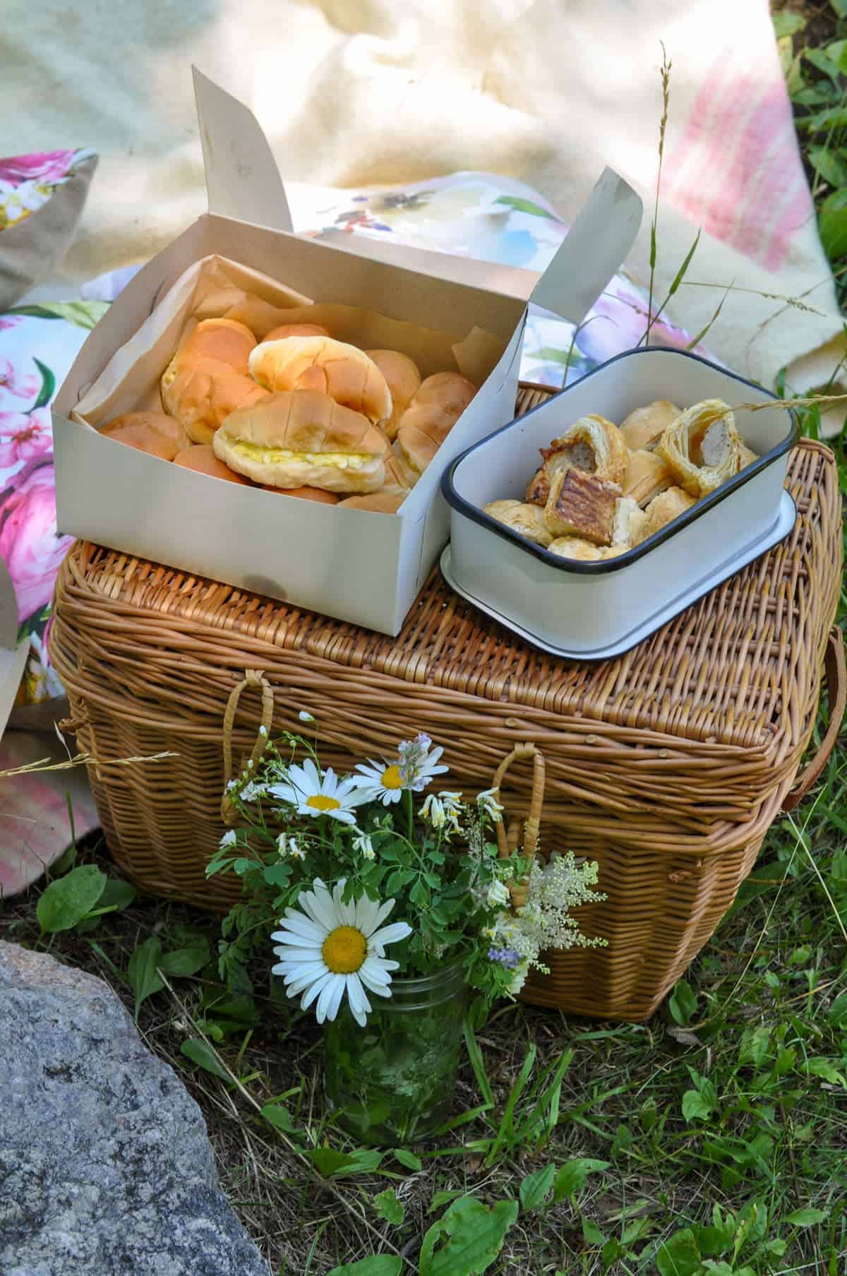 Picnic basket with tea sandwiches and sausage rolls for a tea party picnic.