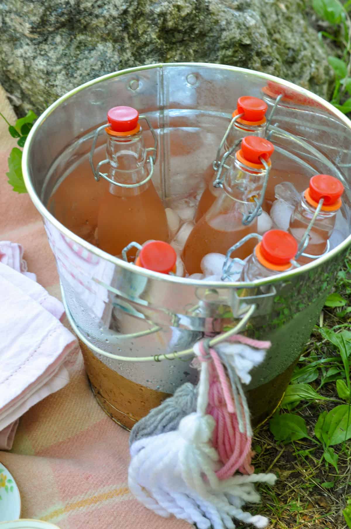 Lemonade bottles chilling in a galvanized bucket of ice at a tea party picnic.