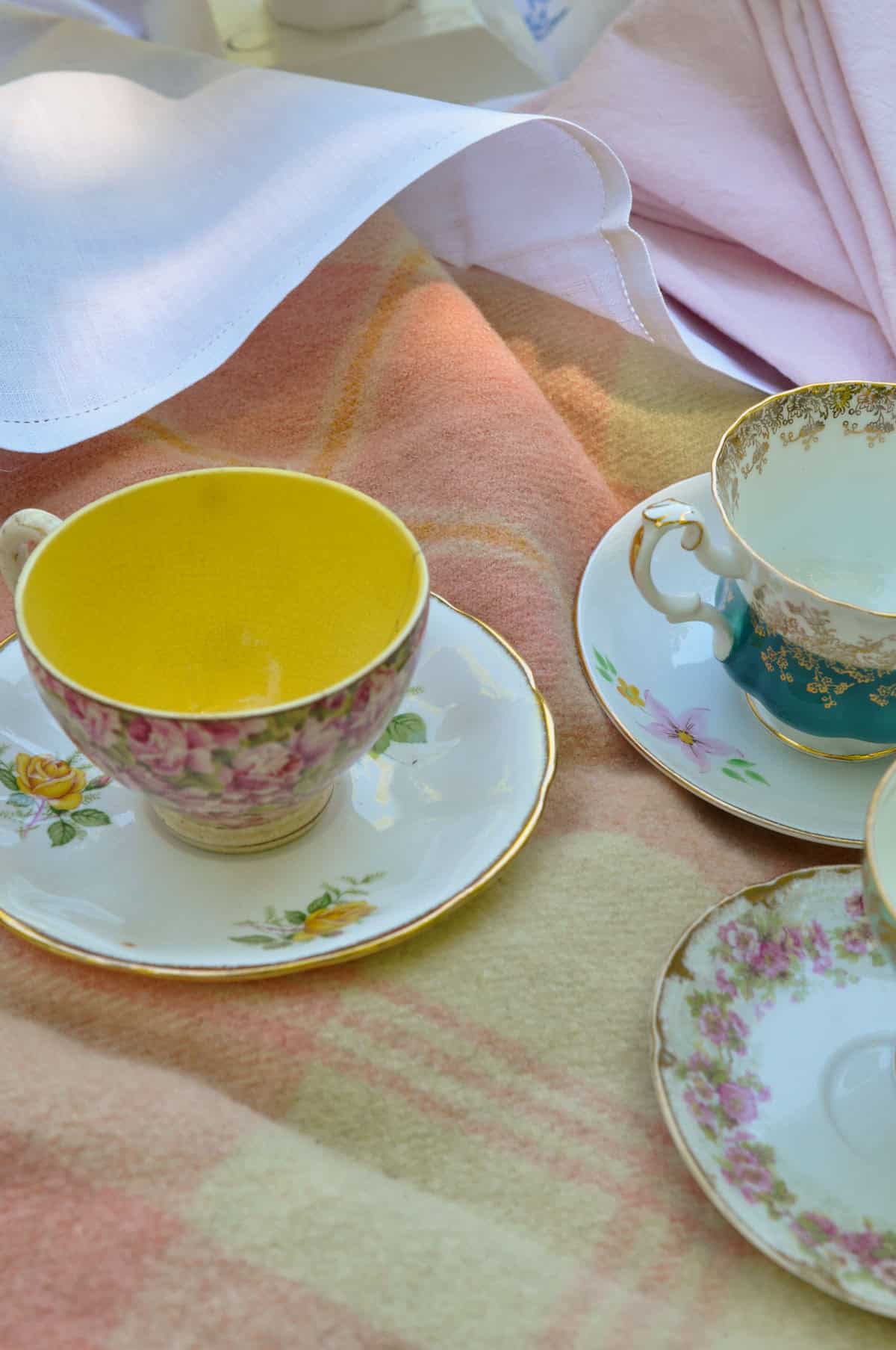 Mismatched vintage floral teacups and saucers at a tea party picnic.