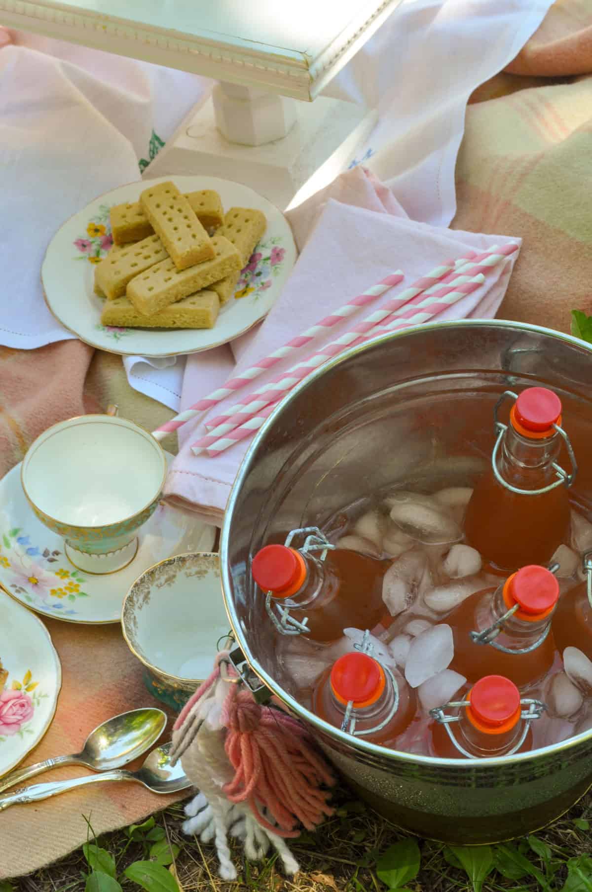 Lemonade bottles chilling in a bucket with shortbread cookies at a tea party picnic.