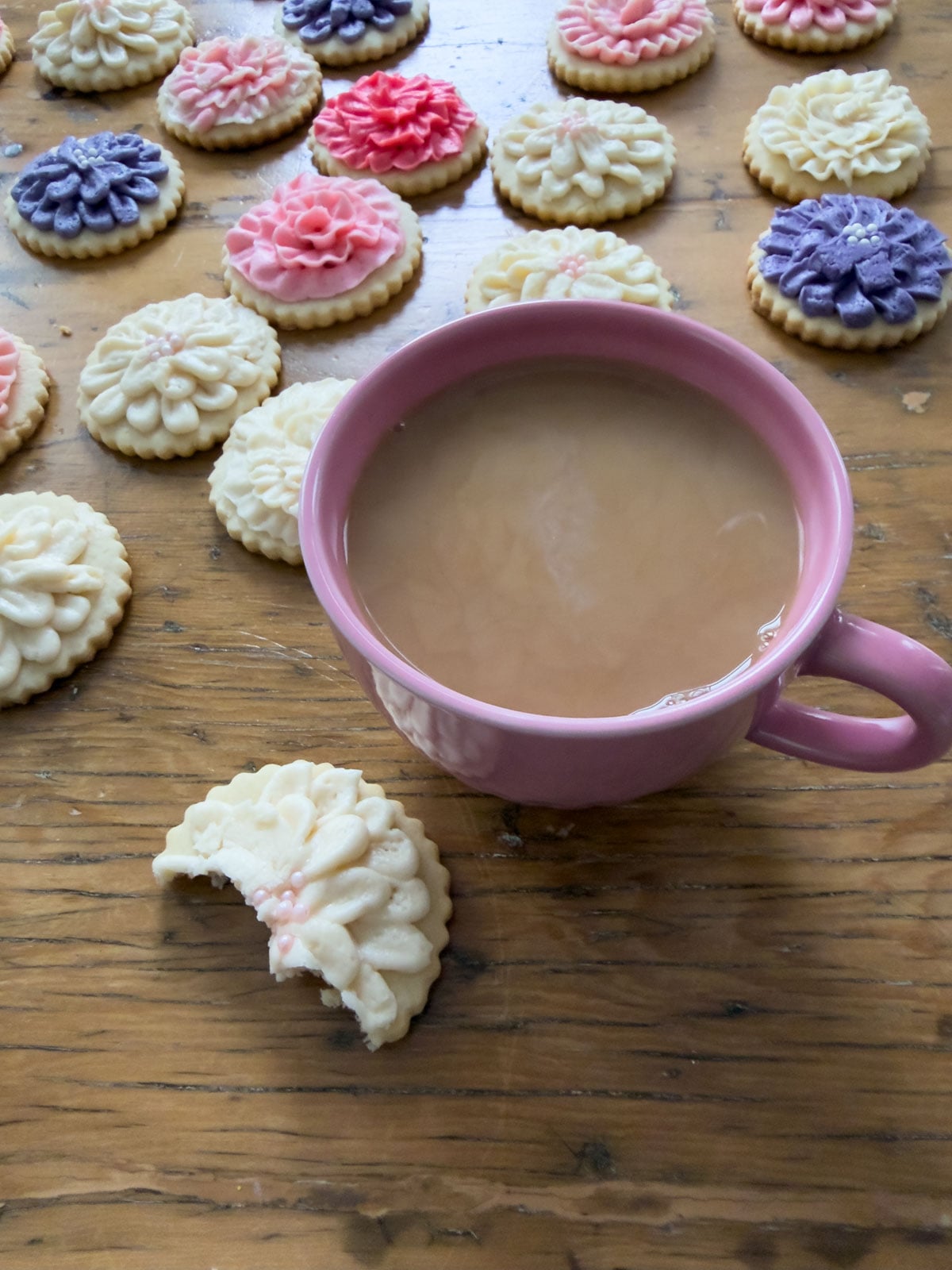 Cut out butter cookies decorated with flower buttercream beside a cup of tea