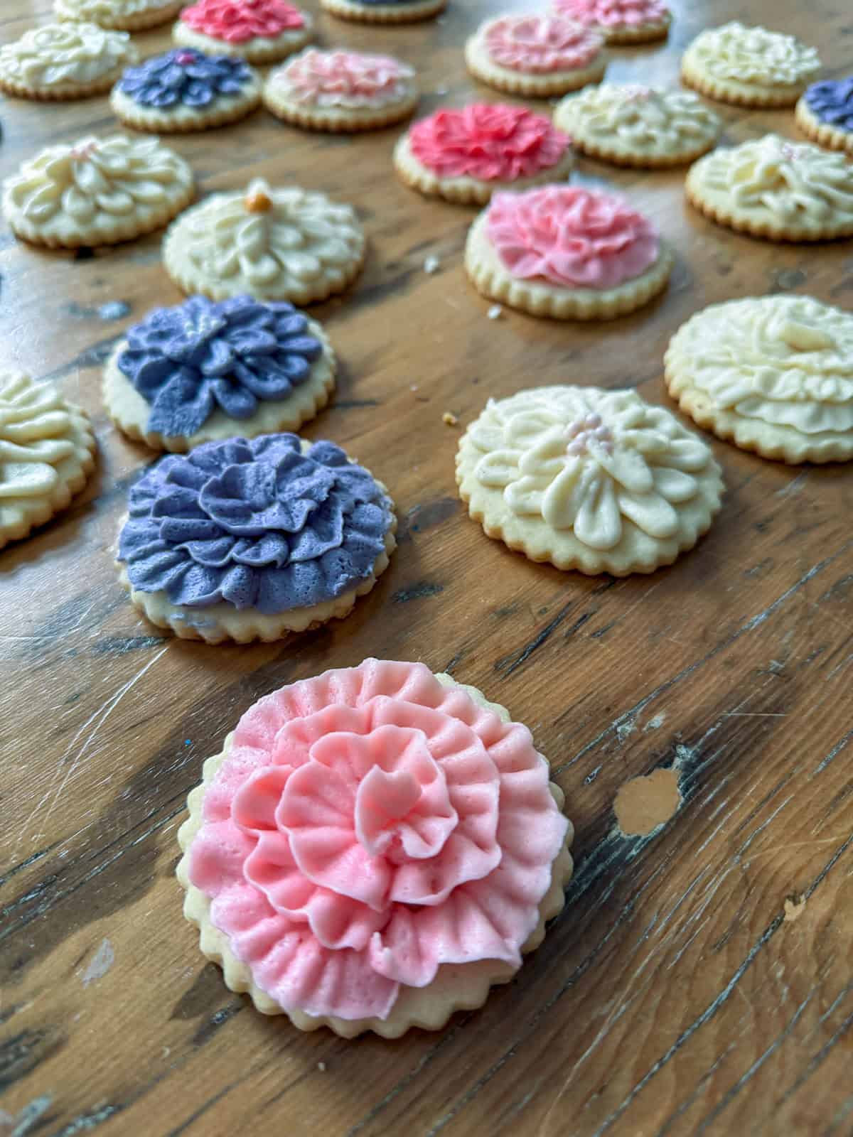 Close up of cut out butter cookies decorated with pink and purple flower buttercream.