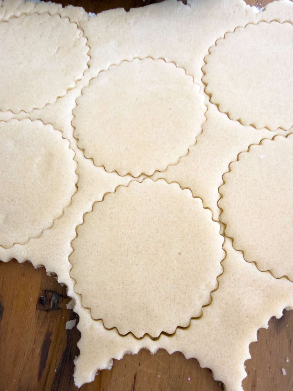 Cut out butter cookie dough cut into rounds with a scalloped cookie cutter.