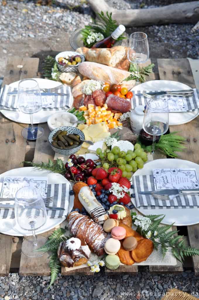 French inspired lakeside picnic with real dishes, and a table full of food incluidng charcuterie, cheese, bread, fruit, and sweets.