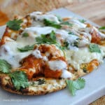 Homemade butter chicken pizza with naan bread, yogurt drizzle, and fresh cilantro.