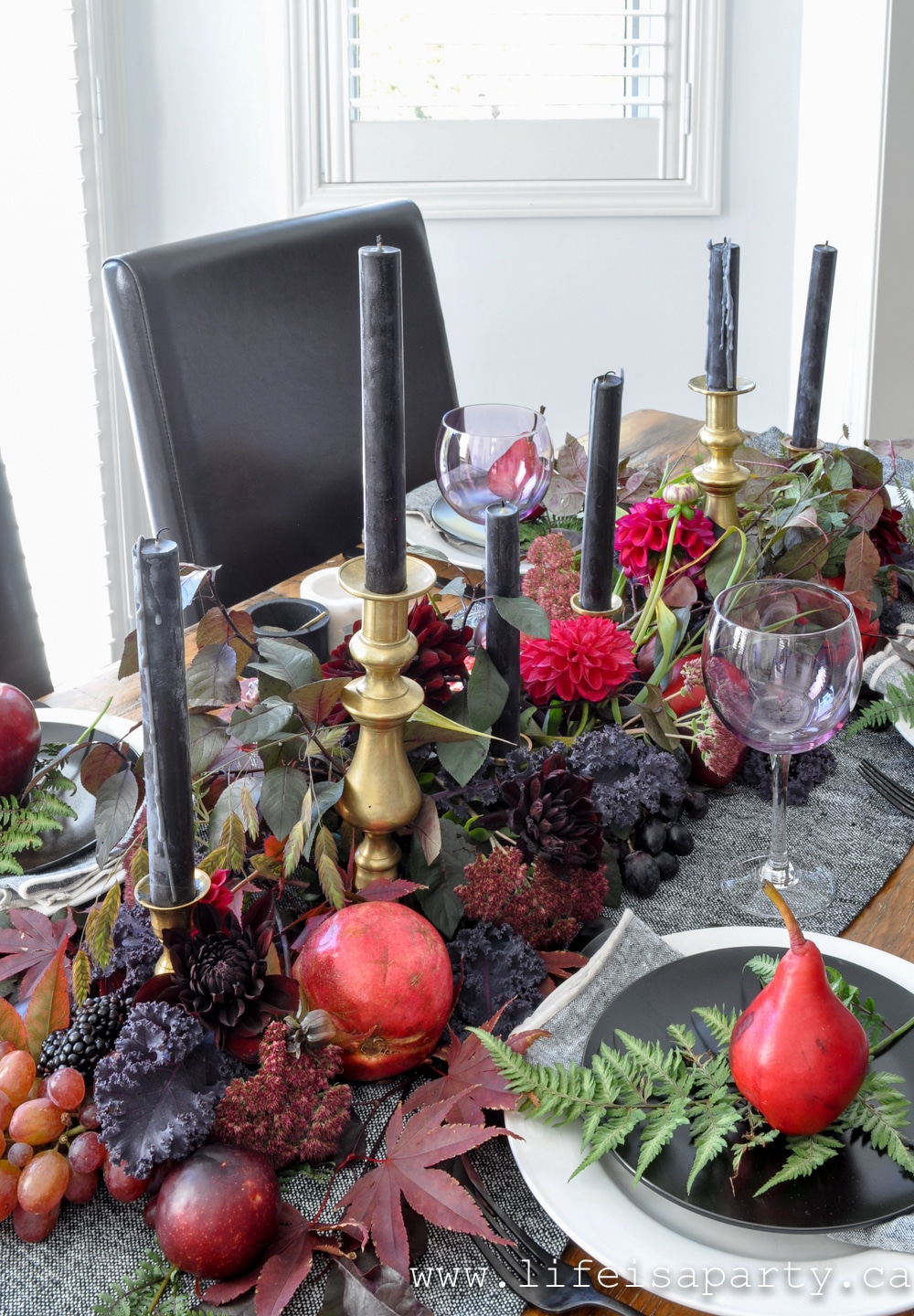 Dark and Moody Thanksgiving Table: purple leaves, dark dahlias, and plums, red pears, apples, pomegranates, and blackberries create the perfect centrepiece.