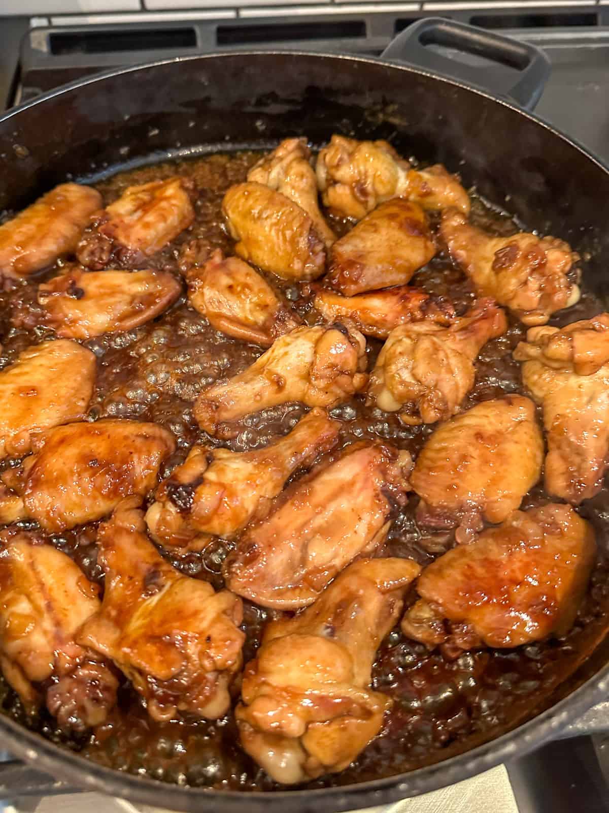 Cooking stove top honey garlic chicken wings in a frying pan with sauce.