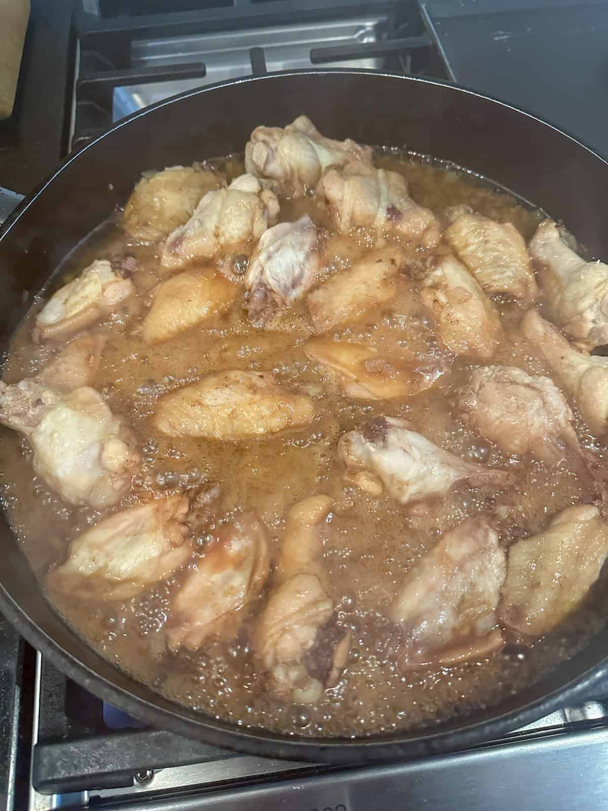 Cooking stove top honey garlic chicken wings in a large frying pan.